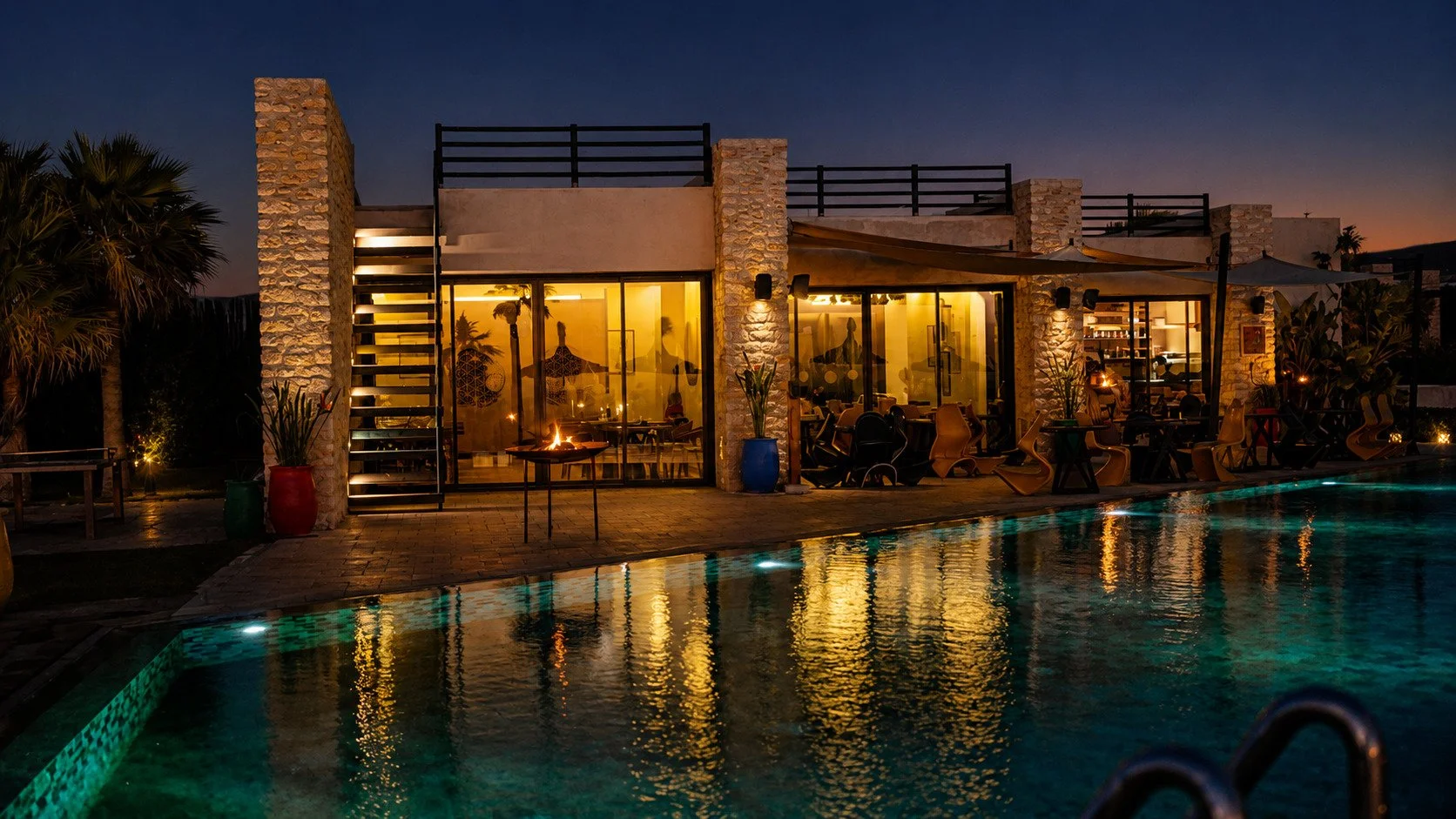 Piscine éclairée au crépuscule avec palmiers — espace détente retraite yoga bien-être Essaouira Maroc 2026
