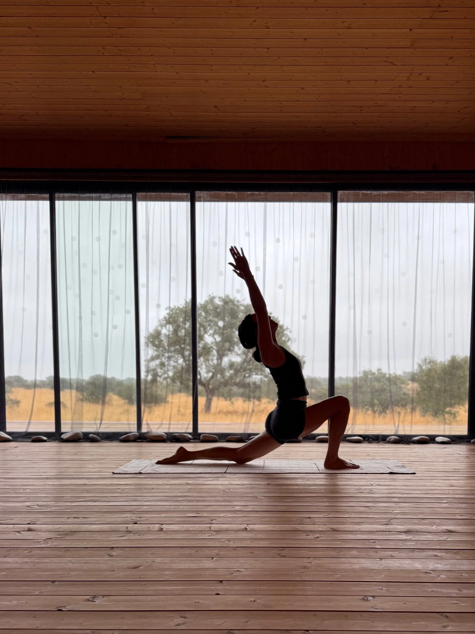 Posture de yoga en silhouette dans le shala vitré, face à la plaine de l'Alentejo