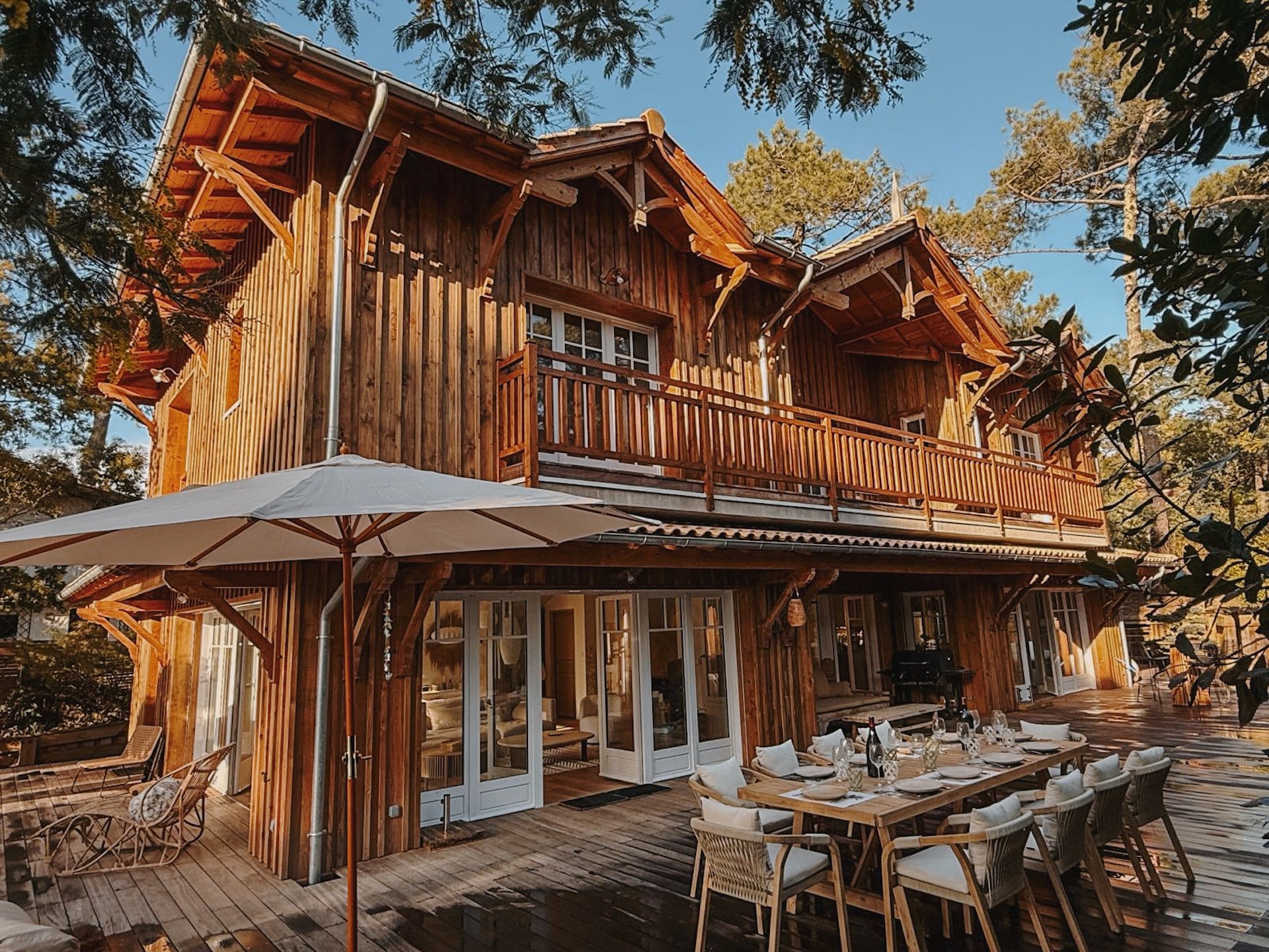 Façade en bois de la maison confidentielle du Cap Ferret, terrasse ombragée et tables dressées — surf camp yoga au cœur des Landes