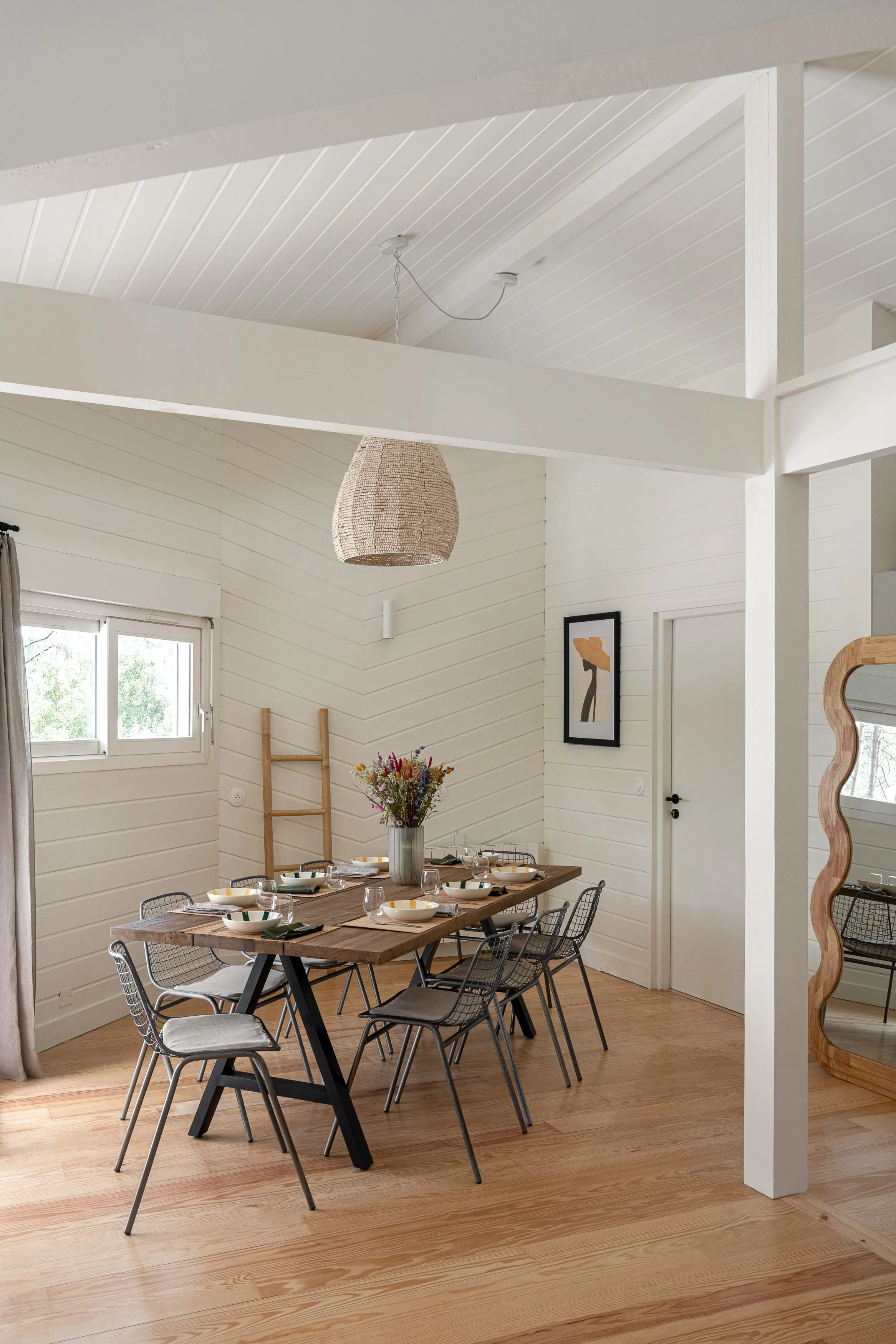 Grande table en bois entourée de chaises design dans une maison lumineuse. Un espace de repas convivial pour partager des repas sains lors de la retraite yoga et surf.