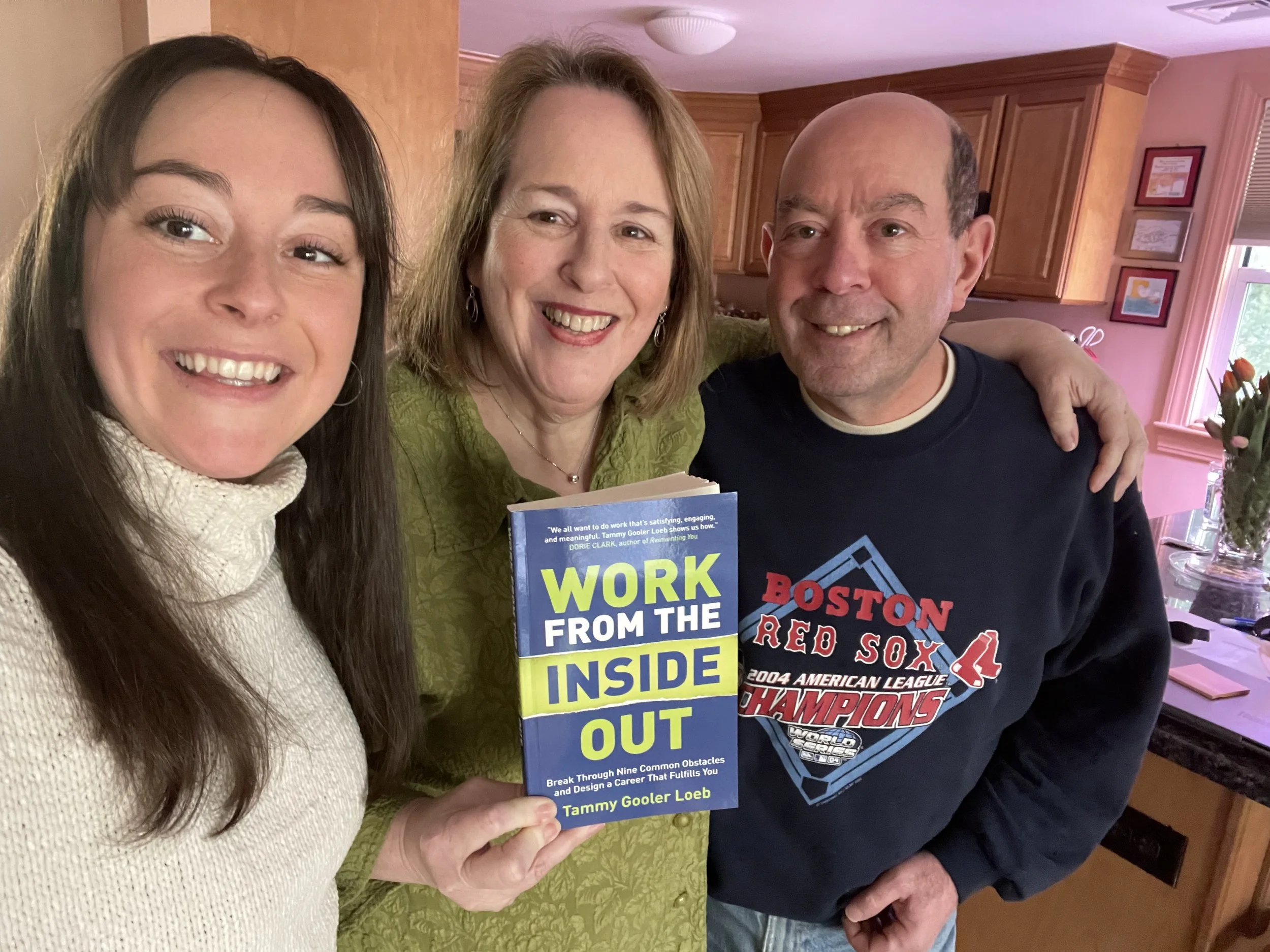 Tammy smiling and holding her book with her husband and daughter