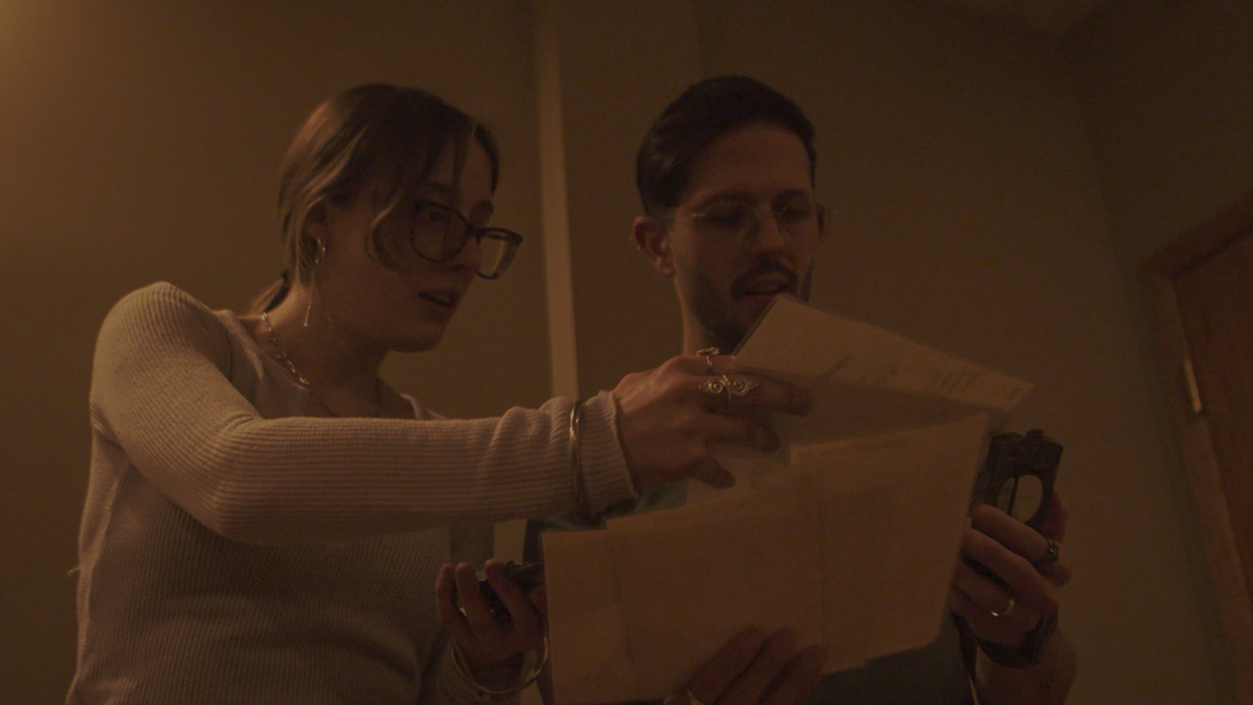 A woman and a man are looking at a piece of paper or a book together in a dimly lit room.