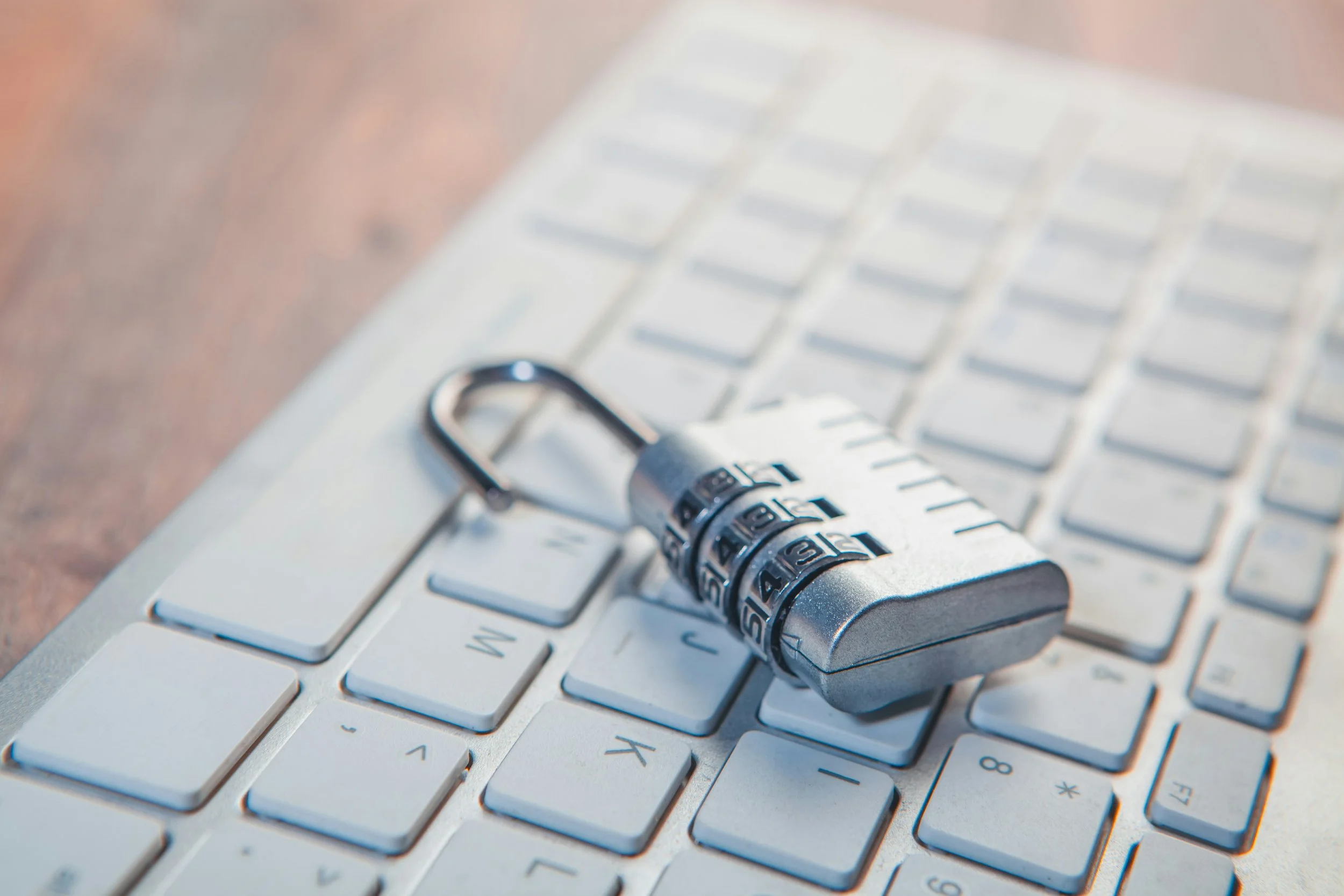 A silver combination padlock rests on the keyboard of a laptop computer. The close-up image symbolizes online security, privacy, password protection, and safeguarding personal information.