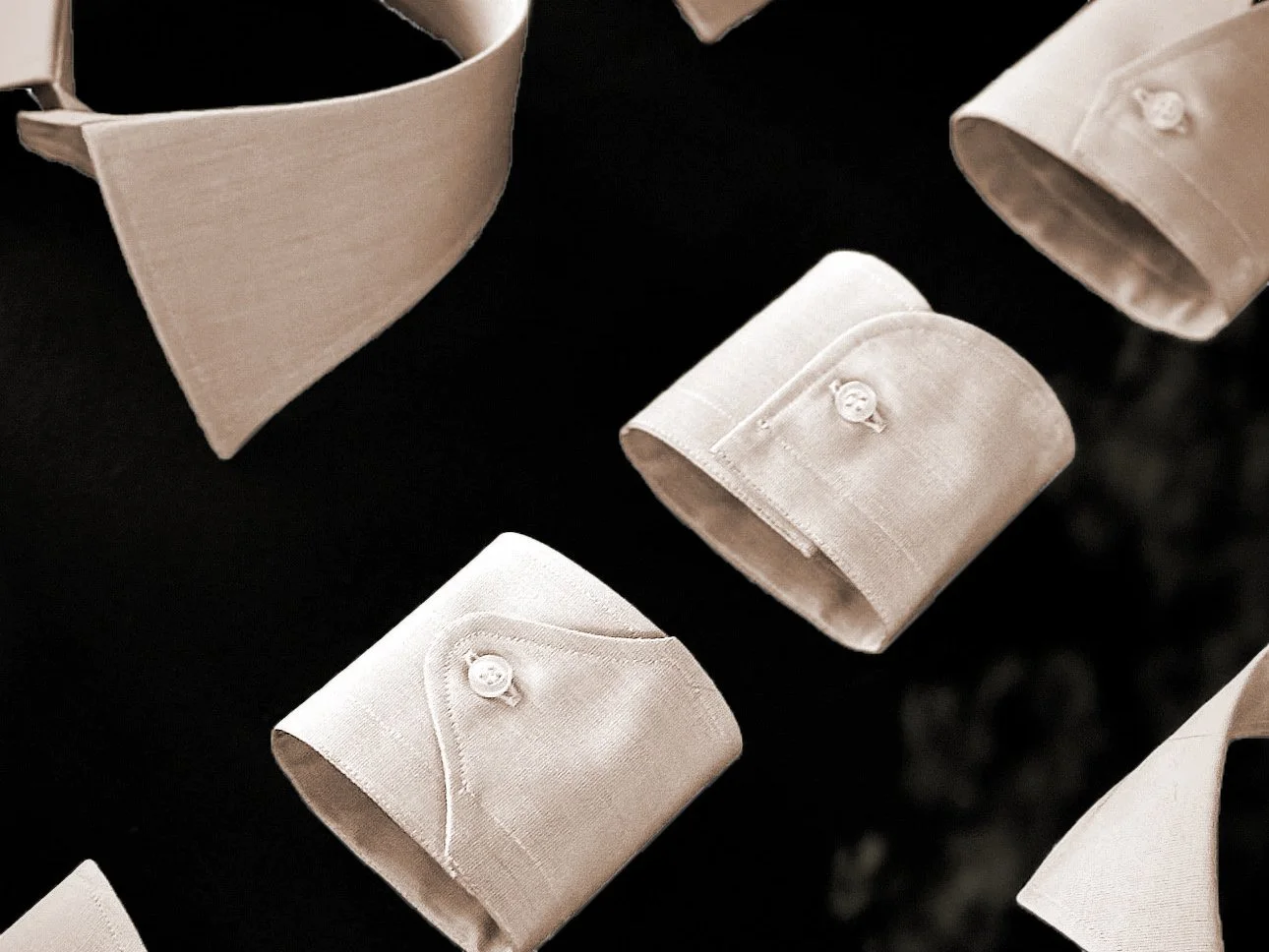Close-up of folded white dress shirts with collar buttons on a black surface.