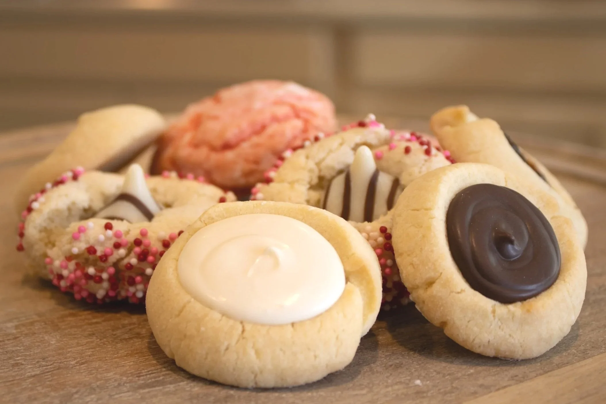 Assorted decorated cookies with white, pink, and dark chocolate icing and sprinkles on a wooden surface.