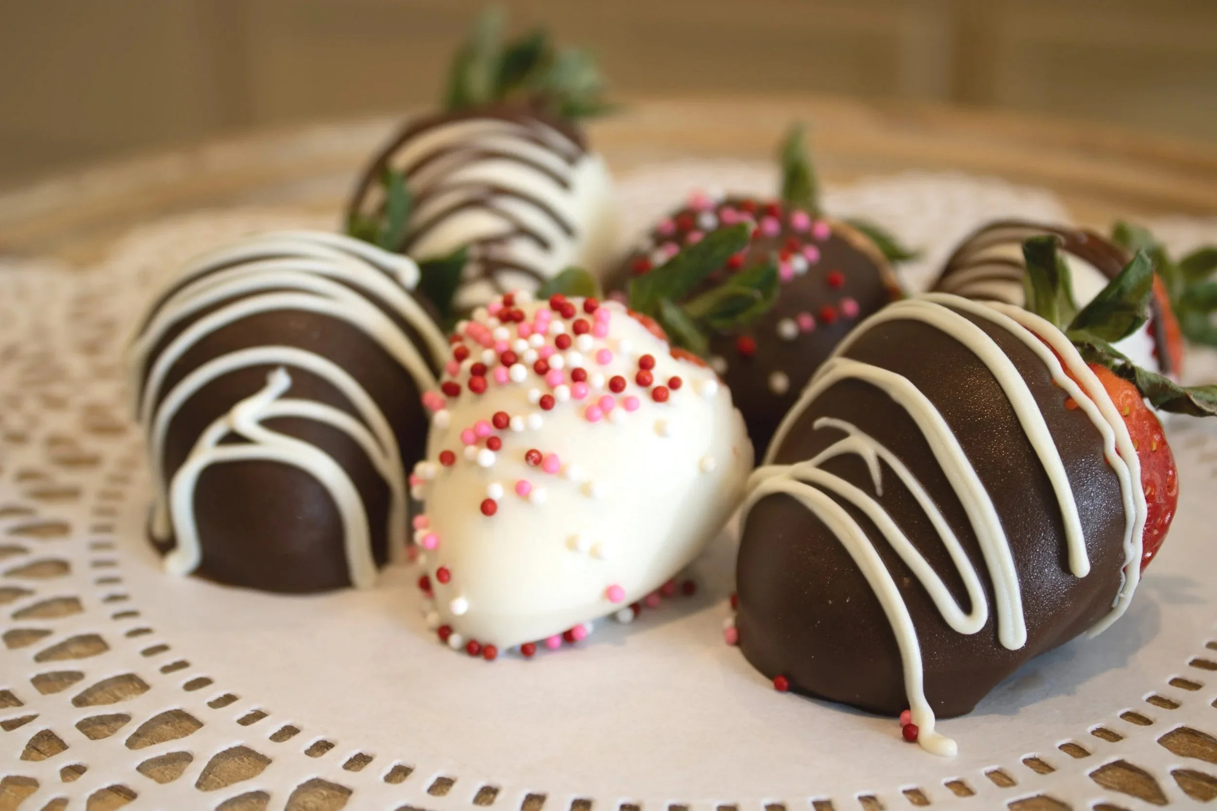 Strawberries dipped in chocolate, decorated with white and pink sprinkles, on a paper doily.