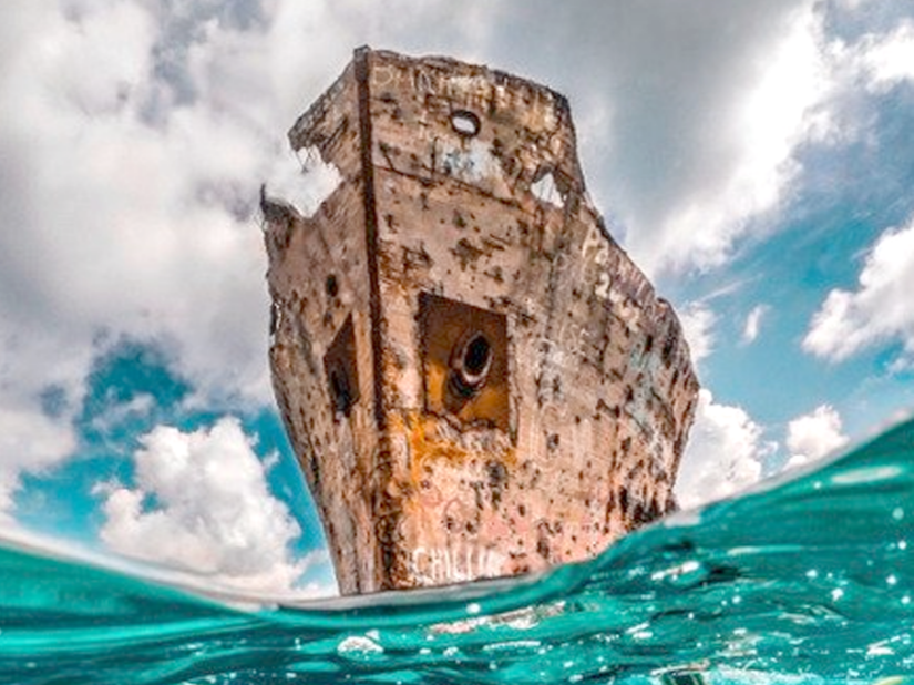 The Sapona shipwreck, located near Bimini, Bahamas, partially submerged in the ocean with a partly cloudy sky in the background.