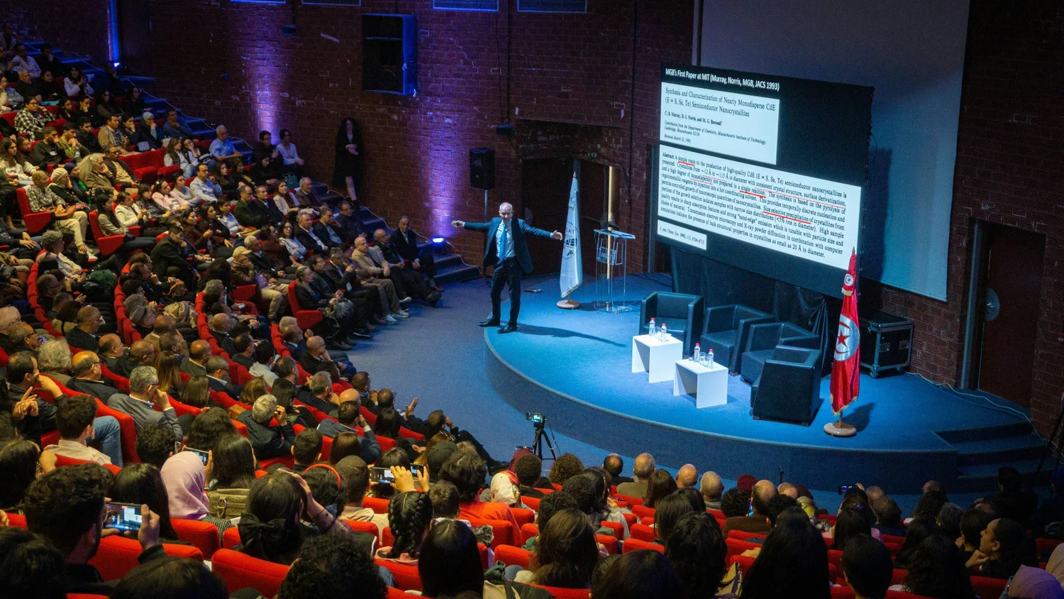 A speaker presenting to a full conference auditorium