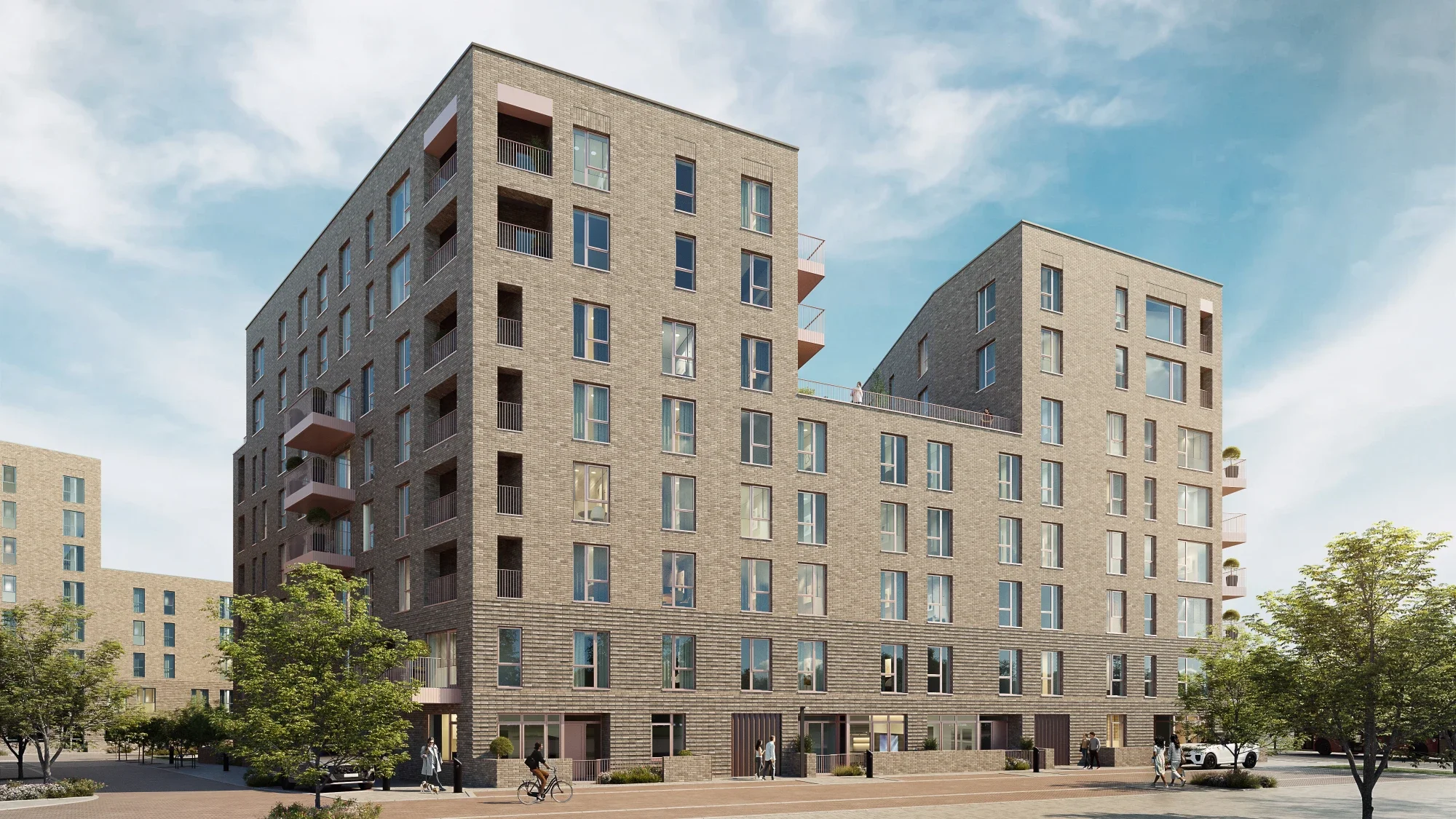 Modern multi-story apartment building with brick facade, large windows, balconies, surrounded by trees and people walking or cycling in the area.