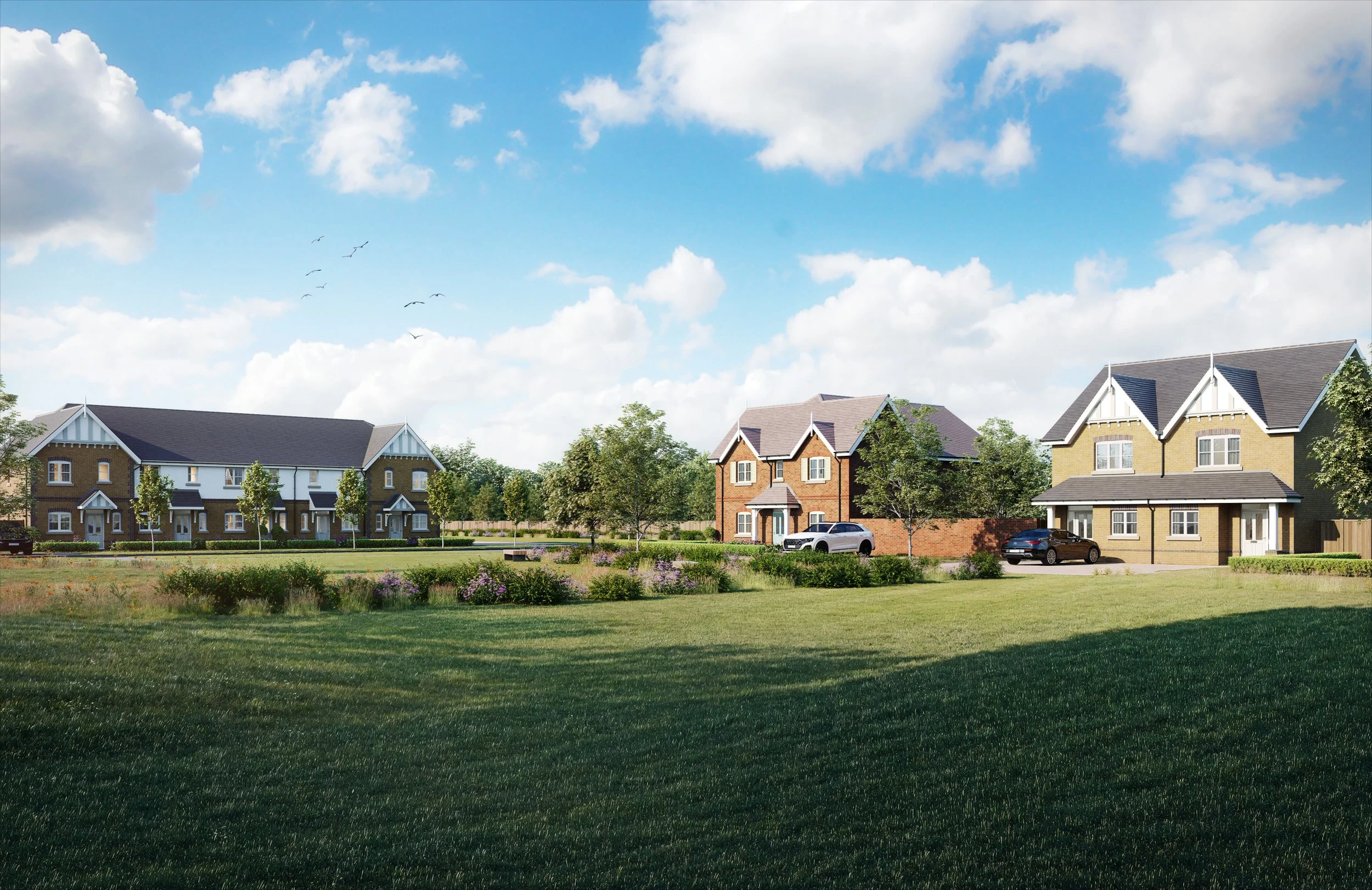 A street scene with green fields in the foreground of hte image, some planting made by bushes and decorative trees with some houses in the background