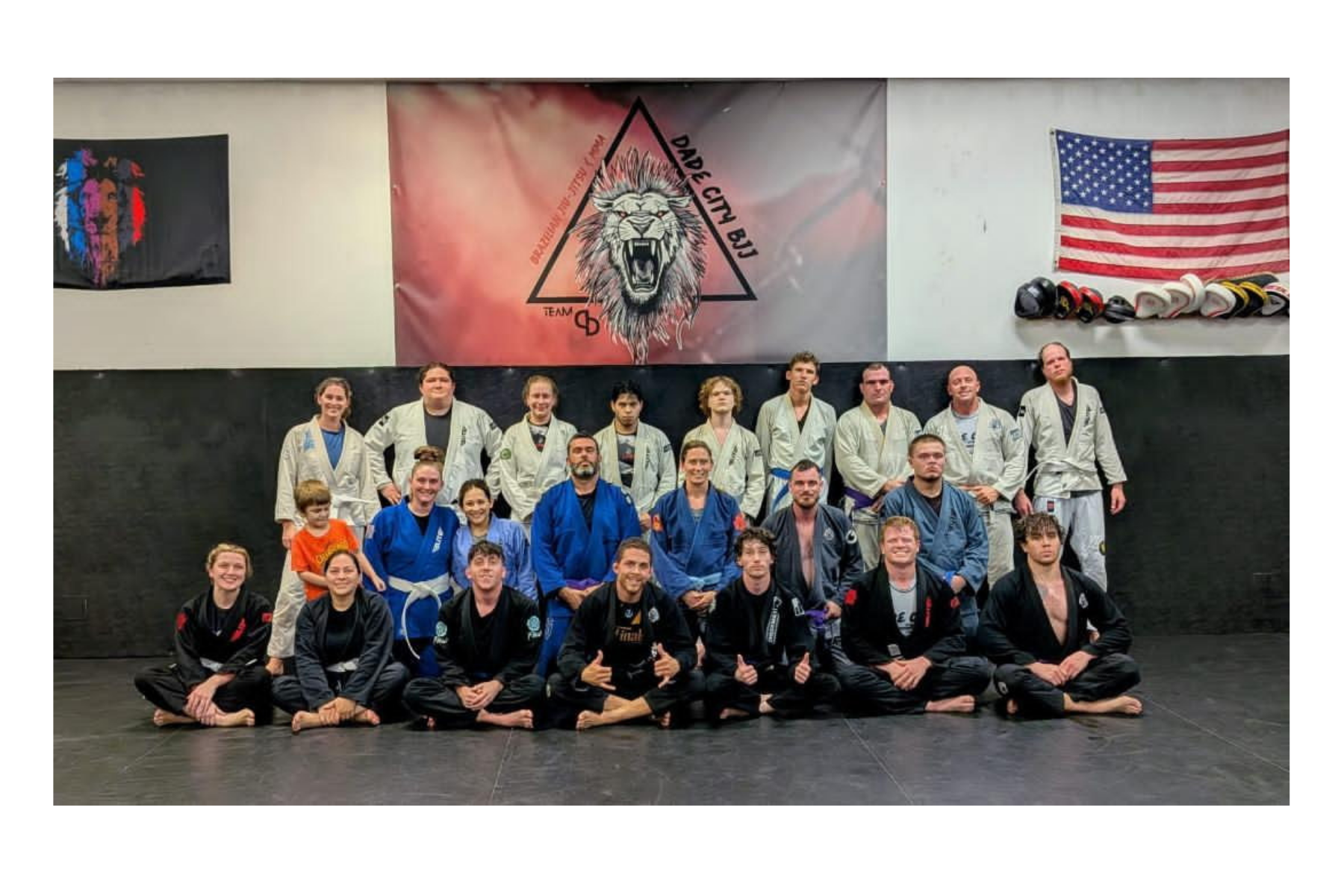 picture of adults in jiu jitsu gis sitting on a large area for training and showing the gyms logo
