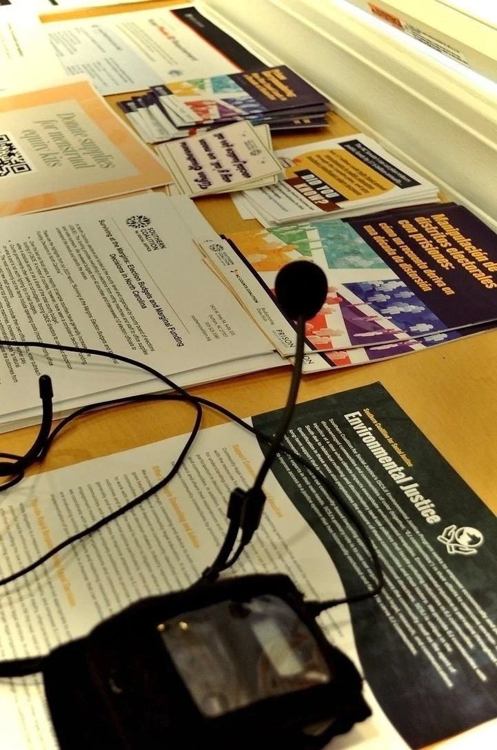 A microphone sits on top of a table with various flyers from different social justice campaigns. The closest one says “environmental justice."