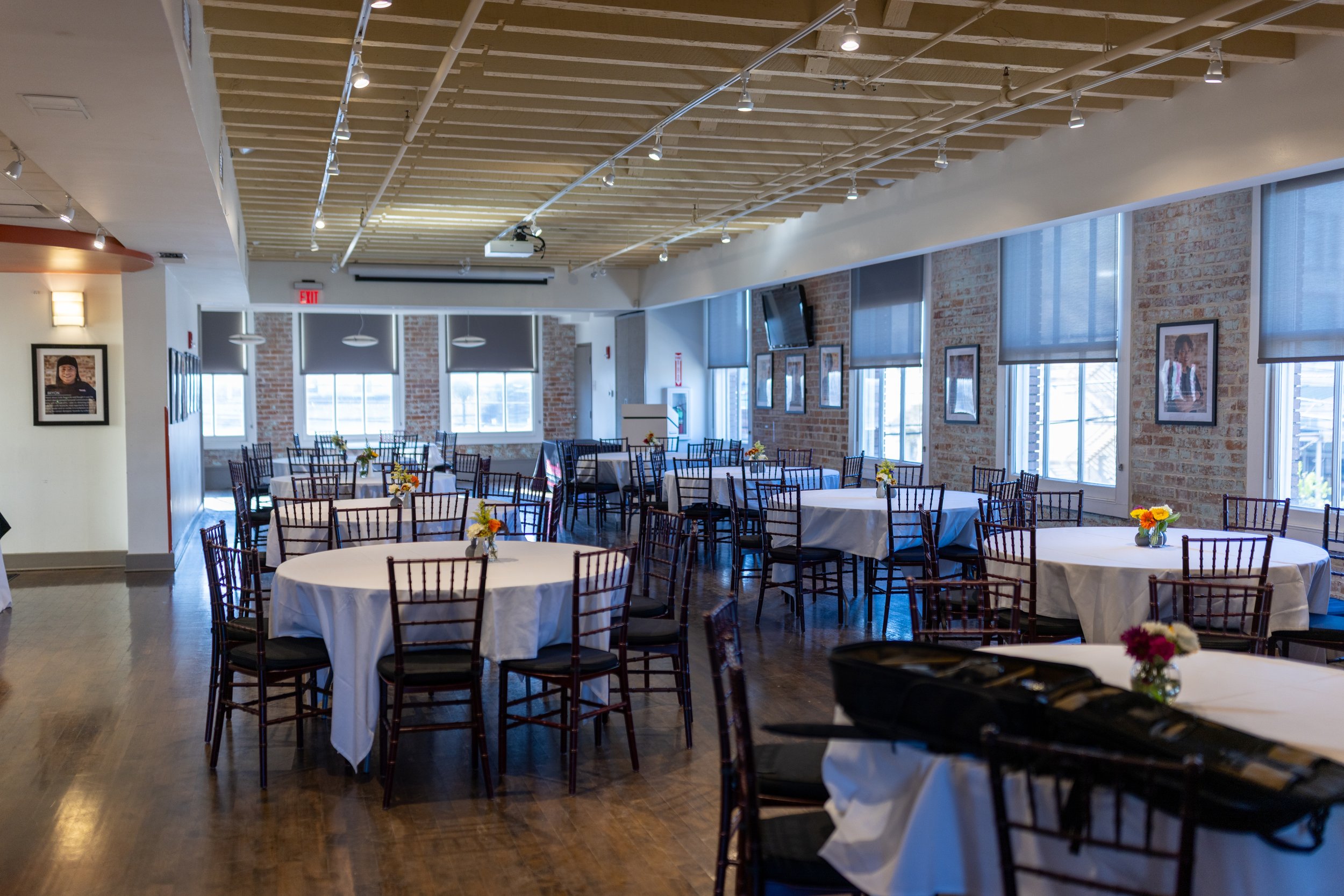 Emeril Lagasse Hospitality Floor. Private Events at Cafe Reconcile. 8 round tables with linens, chairs, and a long table with hot food.
