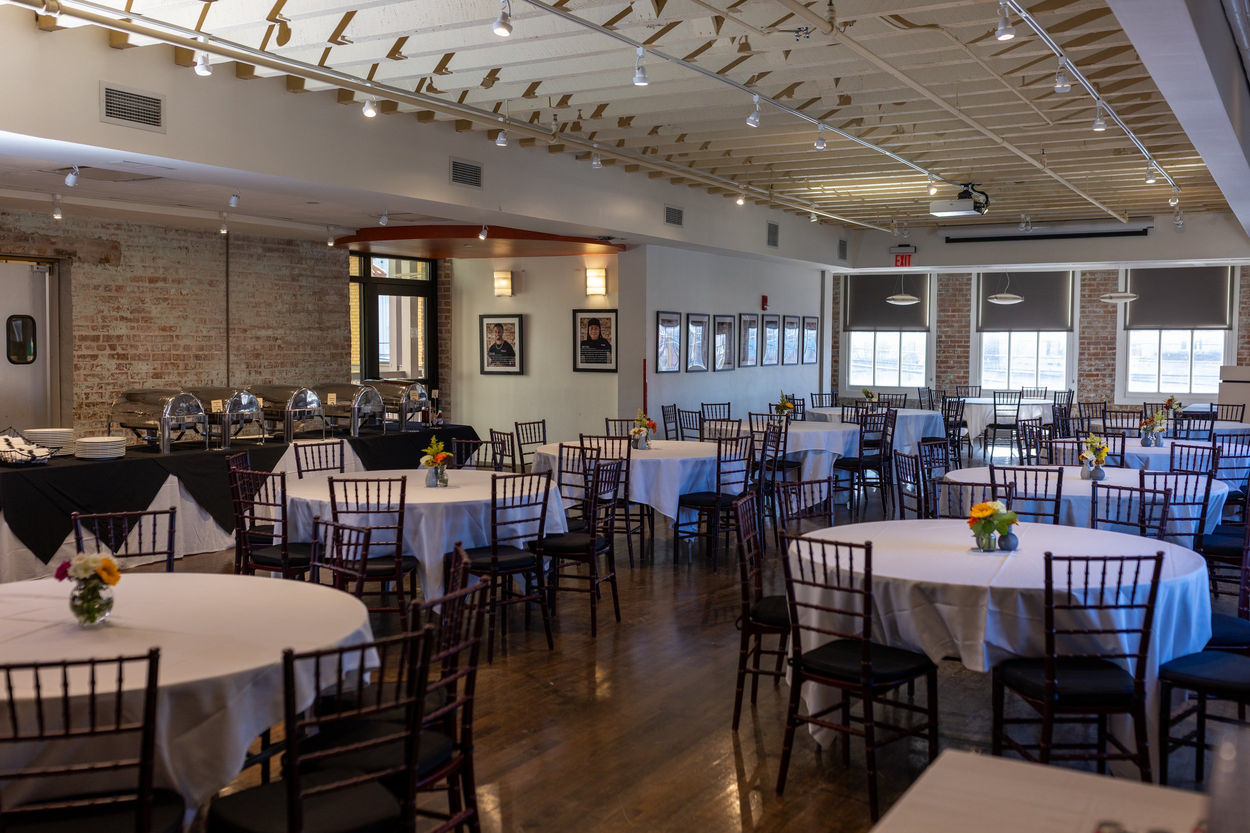 Emeril Lagasse Hospitality Floor. Private Events at Cafe Reconcile. 8 round tables with linens, chairs, and a long table with hot food.