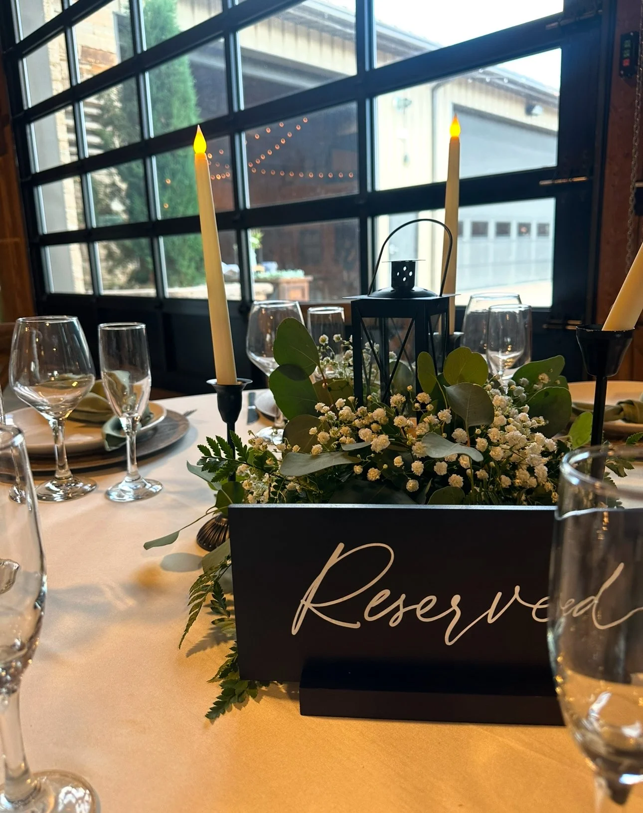 A reserved table at a restaurant with a floral centerpiece, candles, wine glasses, and a 'Reserved' sign.