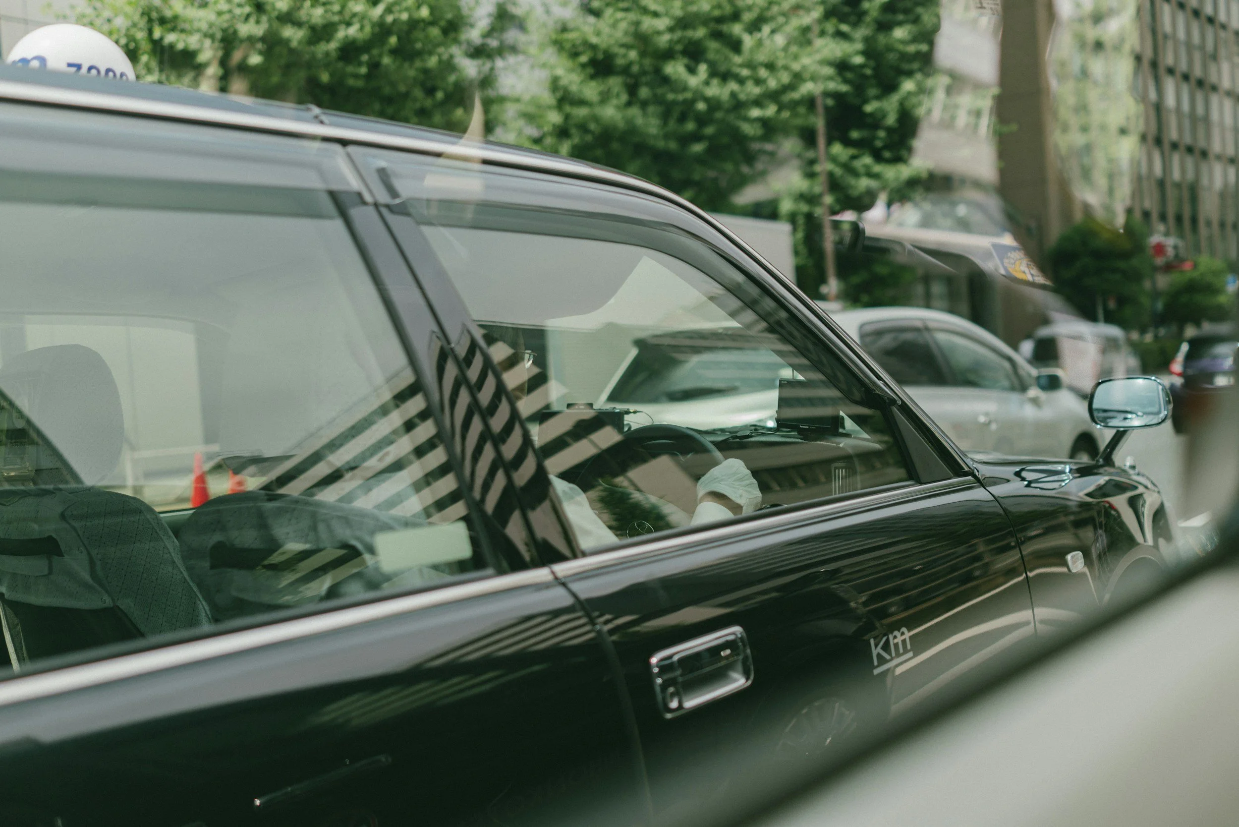 Parked black car with a reflective windshield on a city street, with trees and buildings in the background.