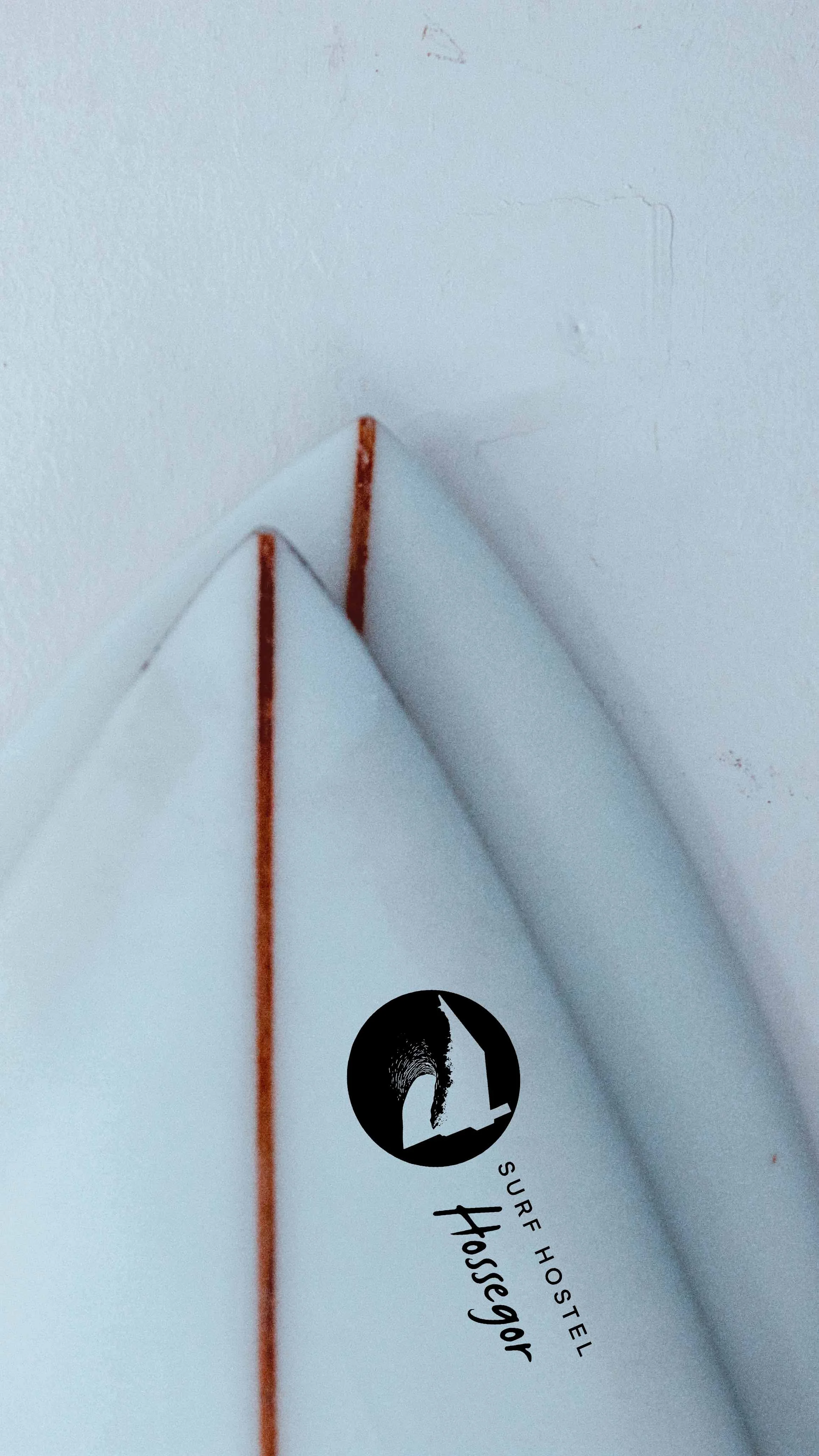 Close-up of the nose of a white surfboard with a black logo reading "Surfer Hostel Housedor" near the corner.