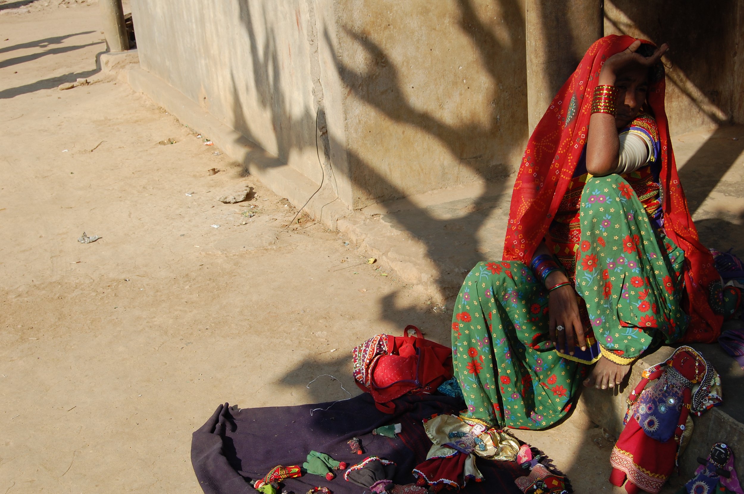 A woman dressed in colorful traditional Indian attire, sitting on a step outside a building, surrounded by handmade jewelry and accessories for sale.