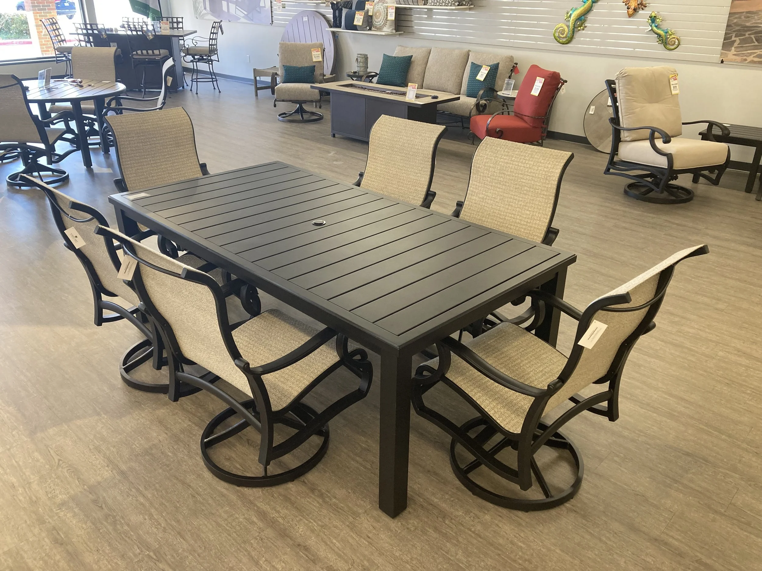 A furniture showroom with a black dining table surrounded by eight beige and black chairs, with various sofas and chairs in the background.