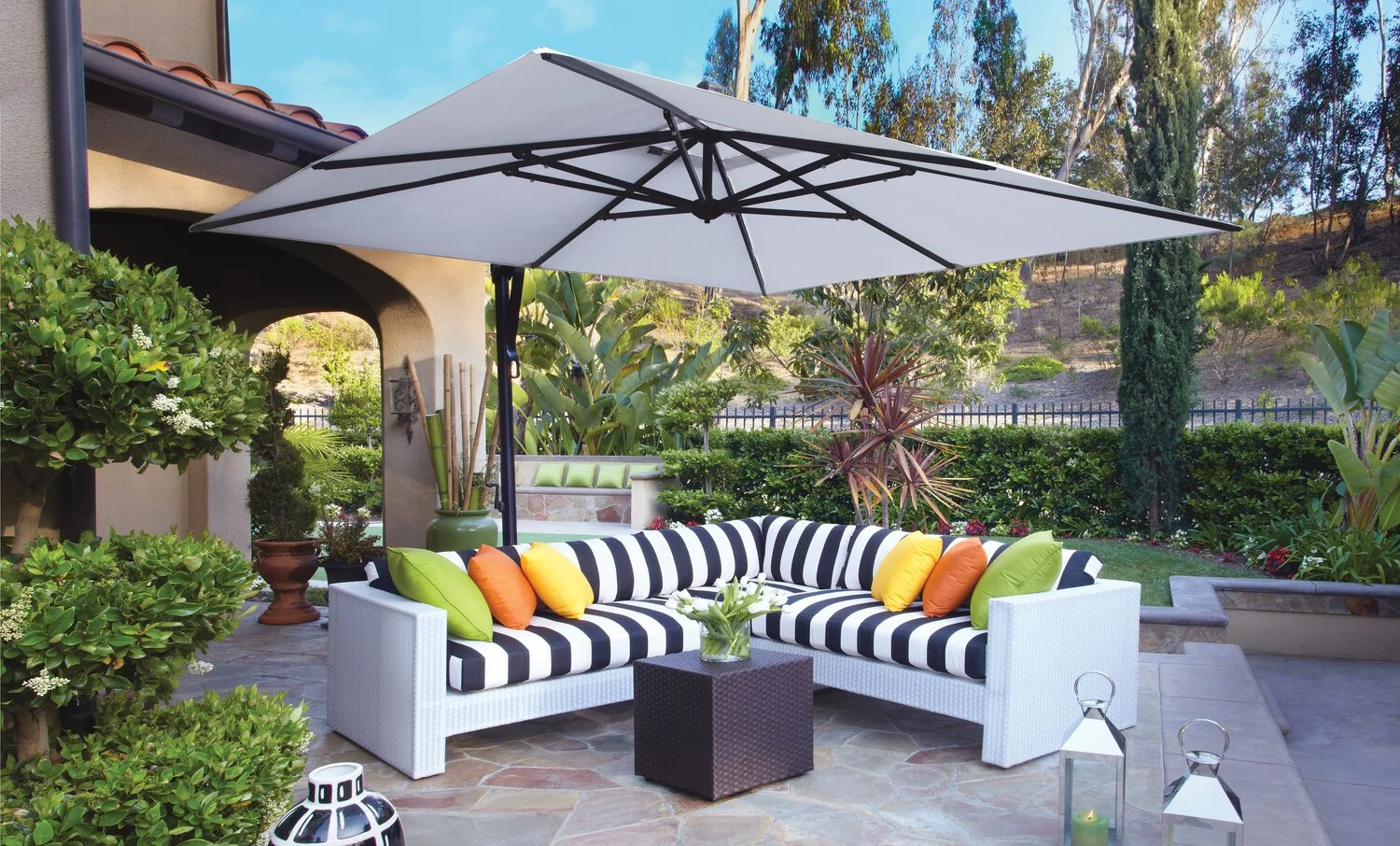 Outdoor patio with striped sofa, colorful pillows, umbrella, plants, lanterns, and table