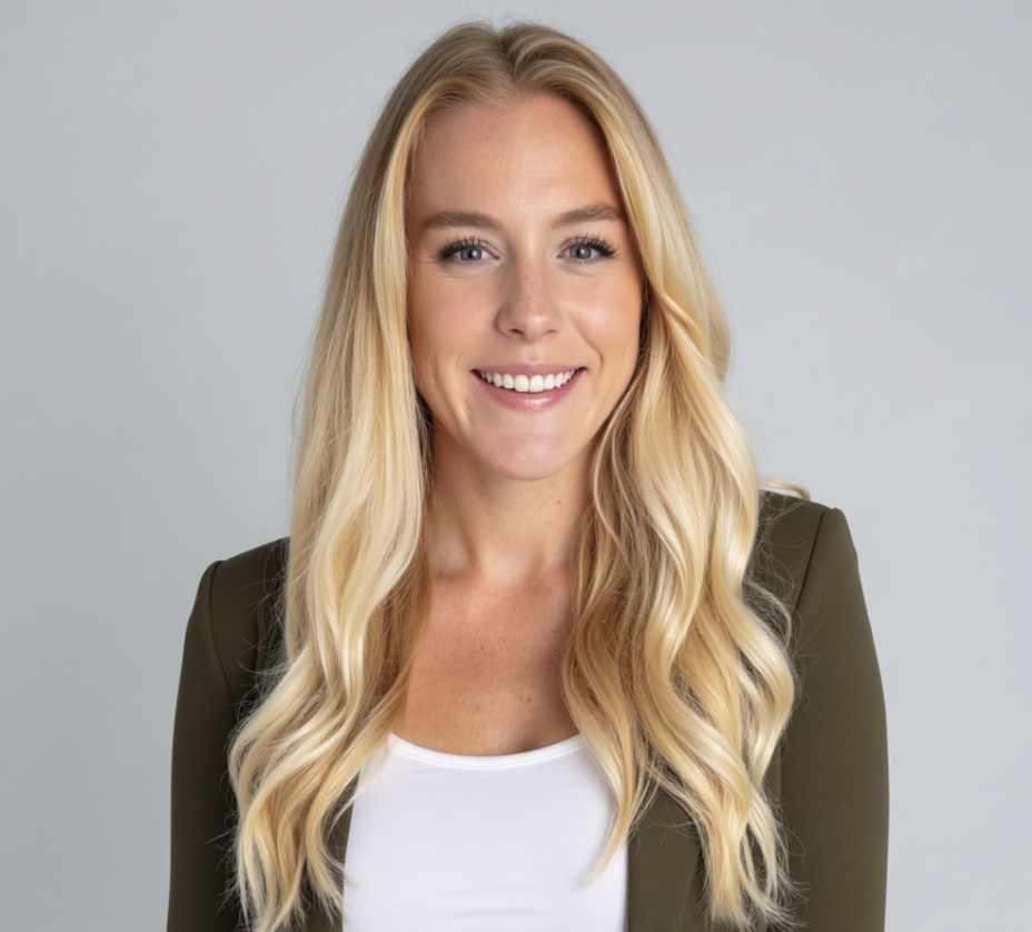 Portrait of a smiling blonde woman with wavy hair, wearing a white top and an olive-green blazer, against a light gray background.