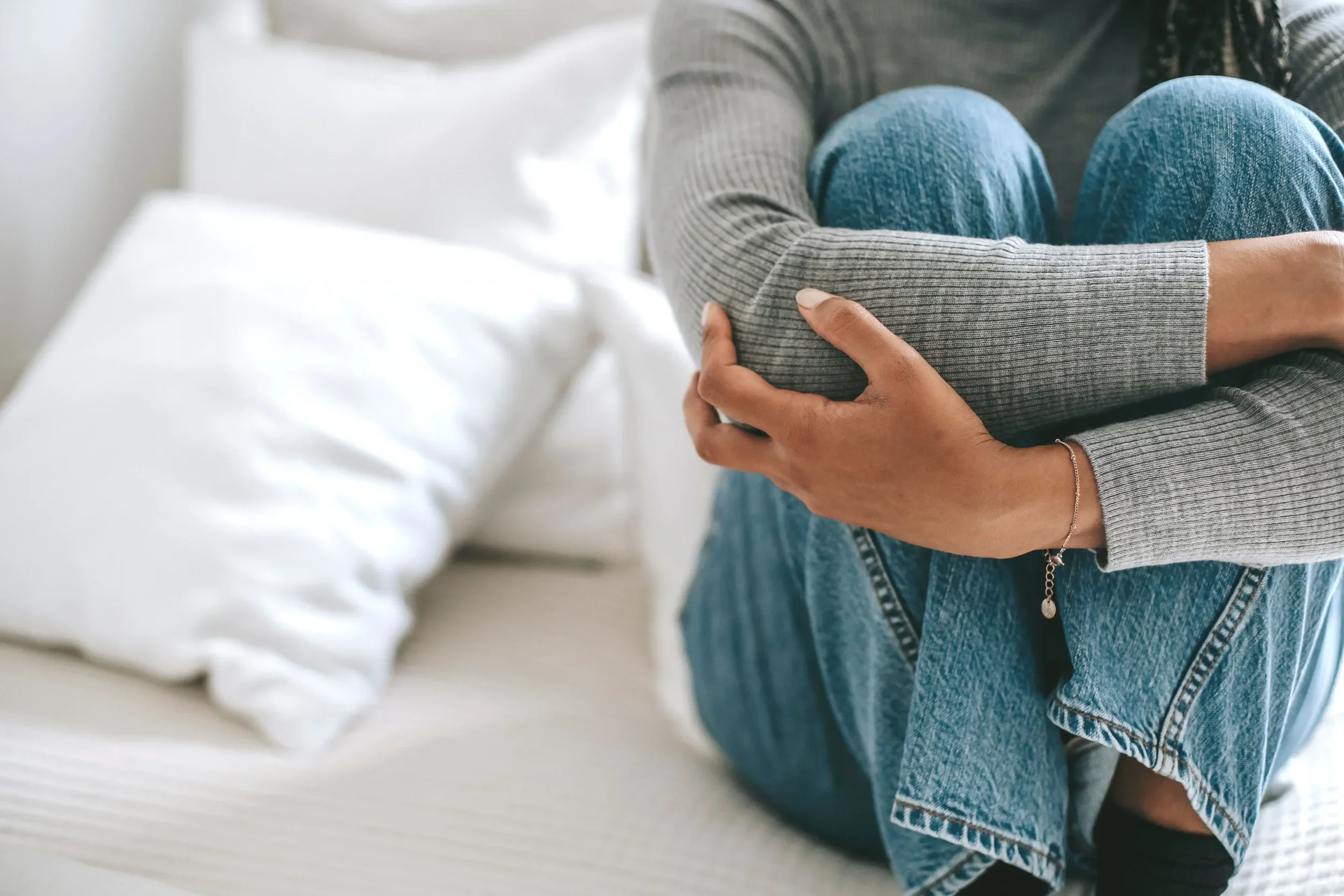 Women sitting on her bed with her hands wrapped around her body feeling her emotions