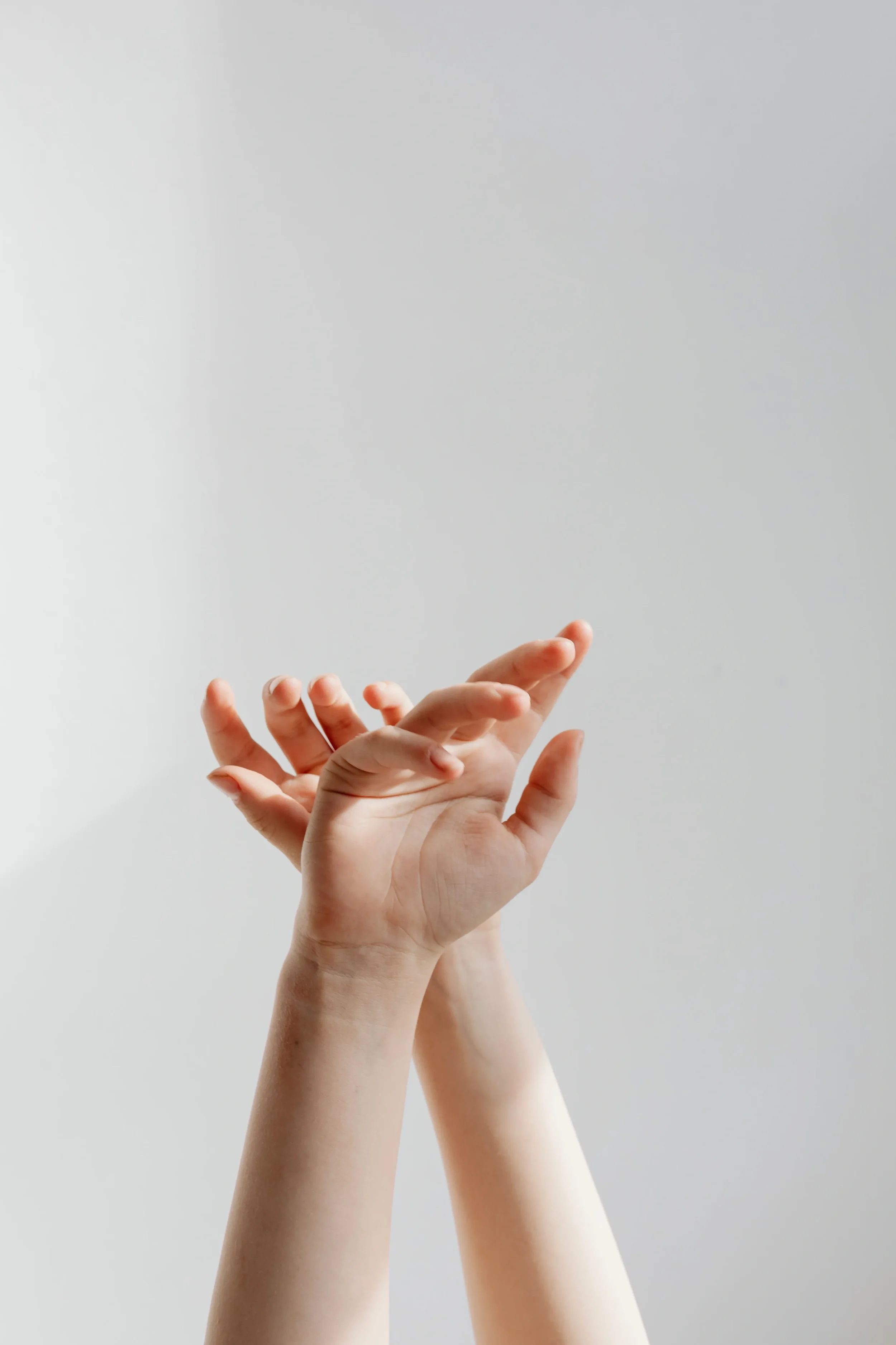 Multiple hands reaching upward with fingers extended against a light gray background.