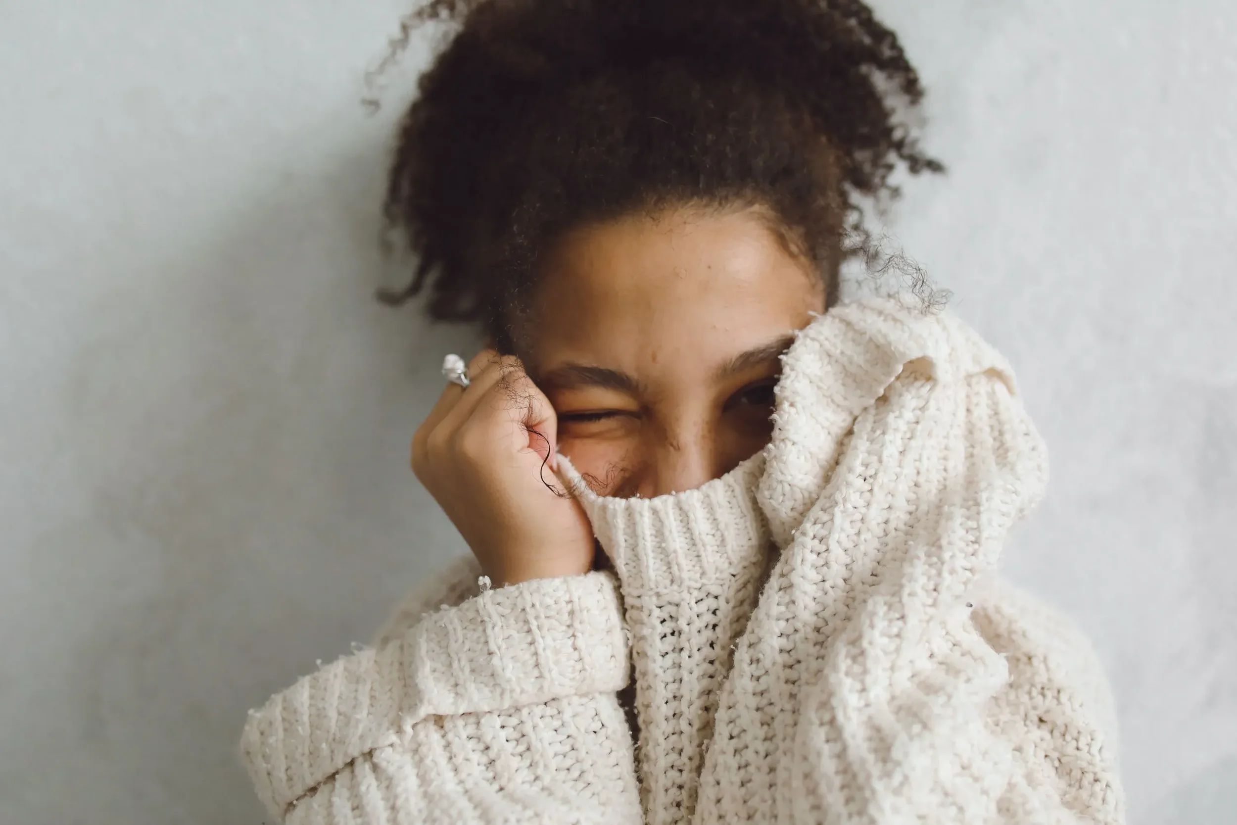 Women in a cozy knit sweater covering half of her face with her sweater looking content, calm and relaxed.