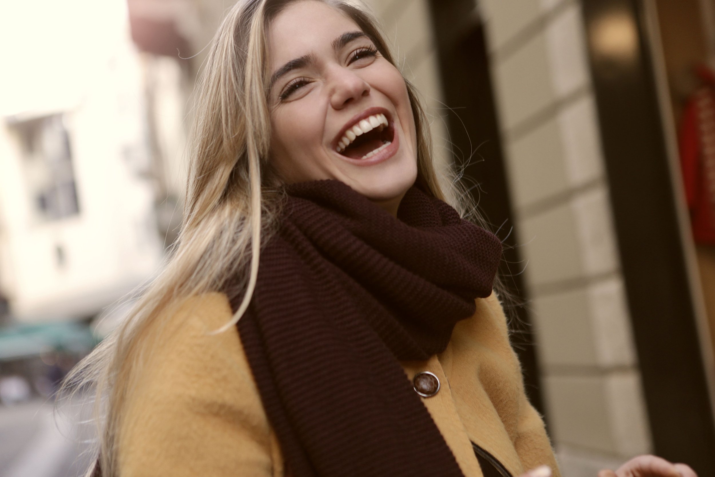A young woman with long blonde hair smiling and laughing in a casual setting.