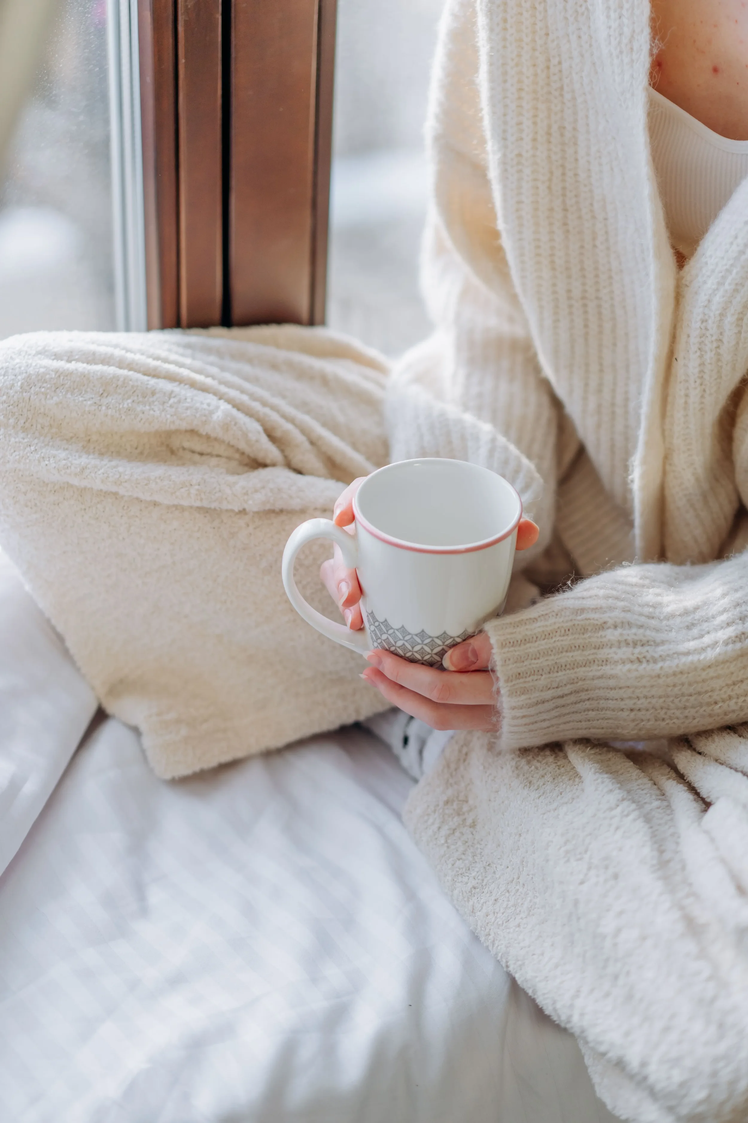 Zoom in on a coffee cup with a girl holding it in fluffy cozy pyjamas.