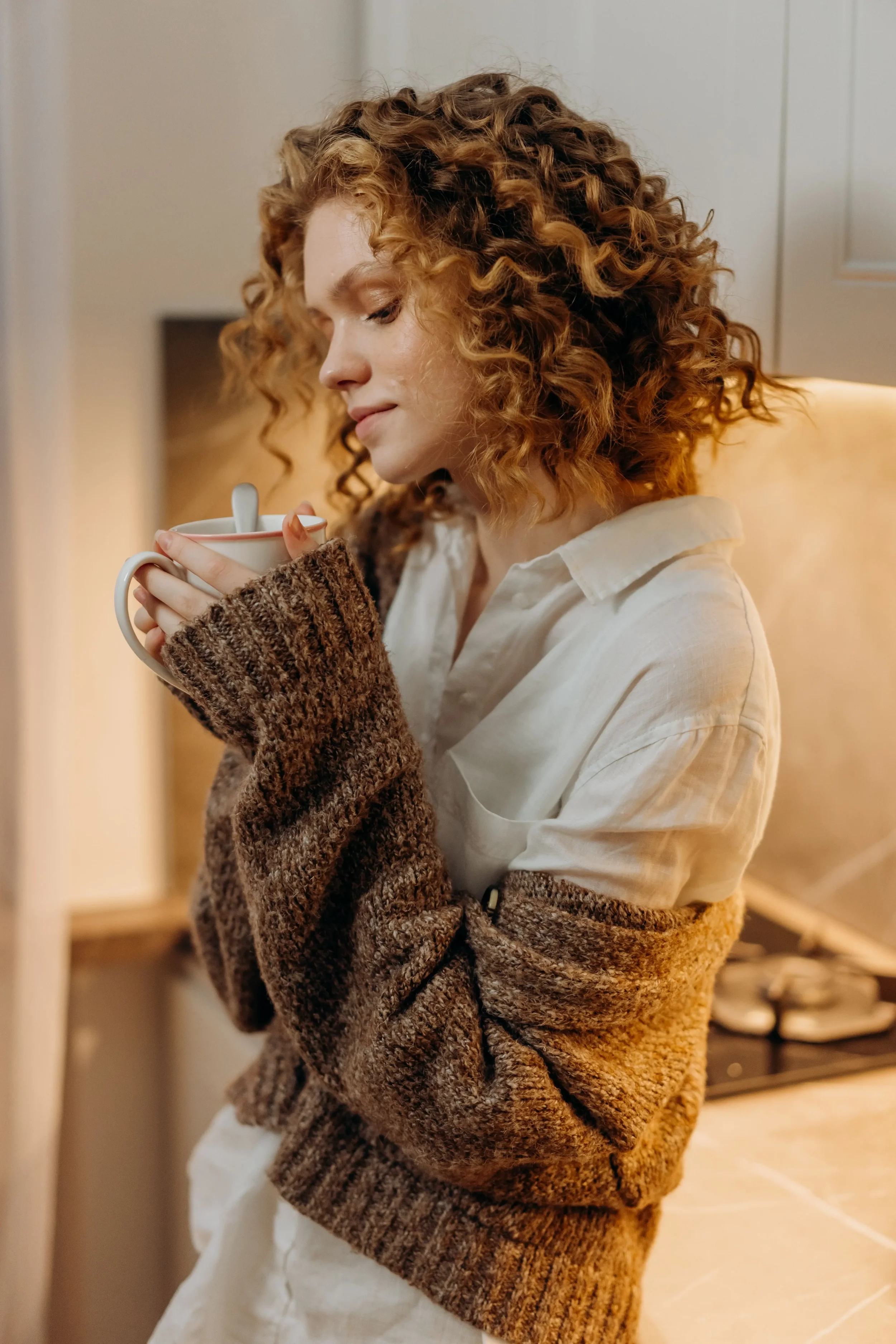 A woman holding a cup of coffee and wearing a brown knitted sweater.