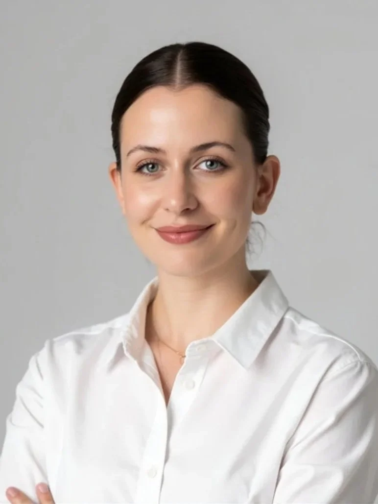 A young woman with dark hair pulled back, smiling and wearing a white button-up shirt against a plain gray background.