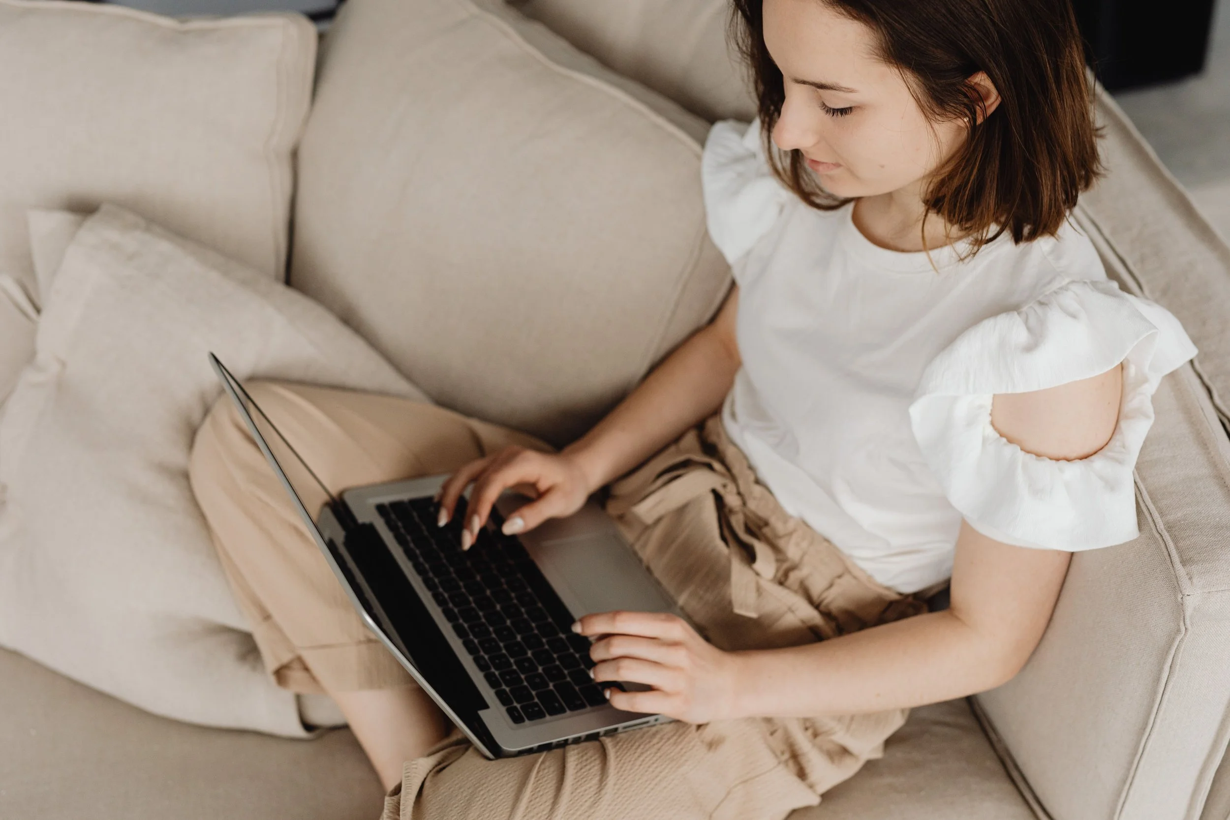 A woman sitting on a beige sofa, using a laptop computer.