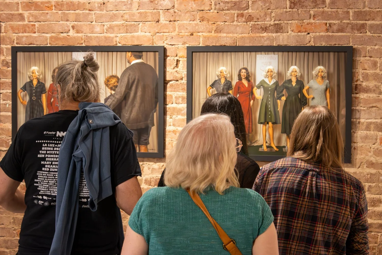 The backs of four gallery guests as they admire two fine art photography portraits featuring a lineup of mannequins with one live model