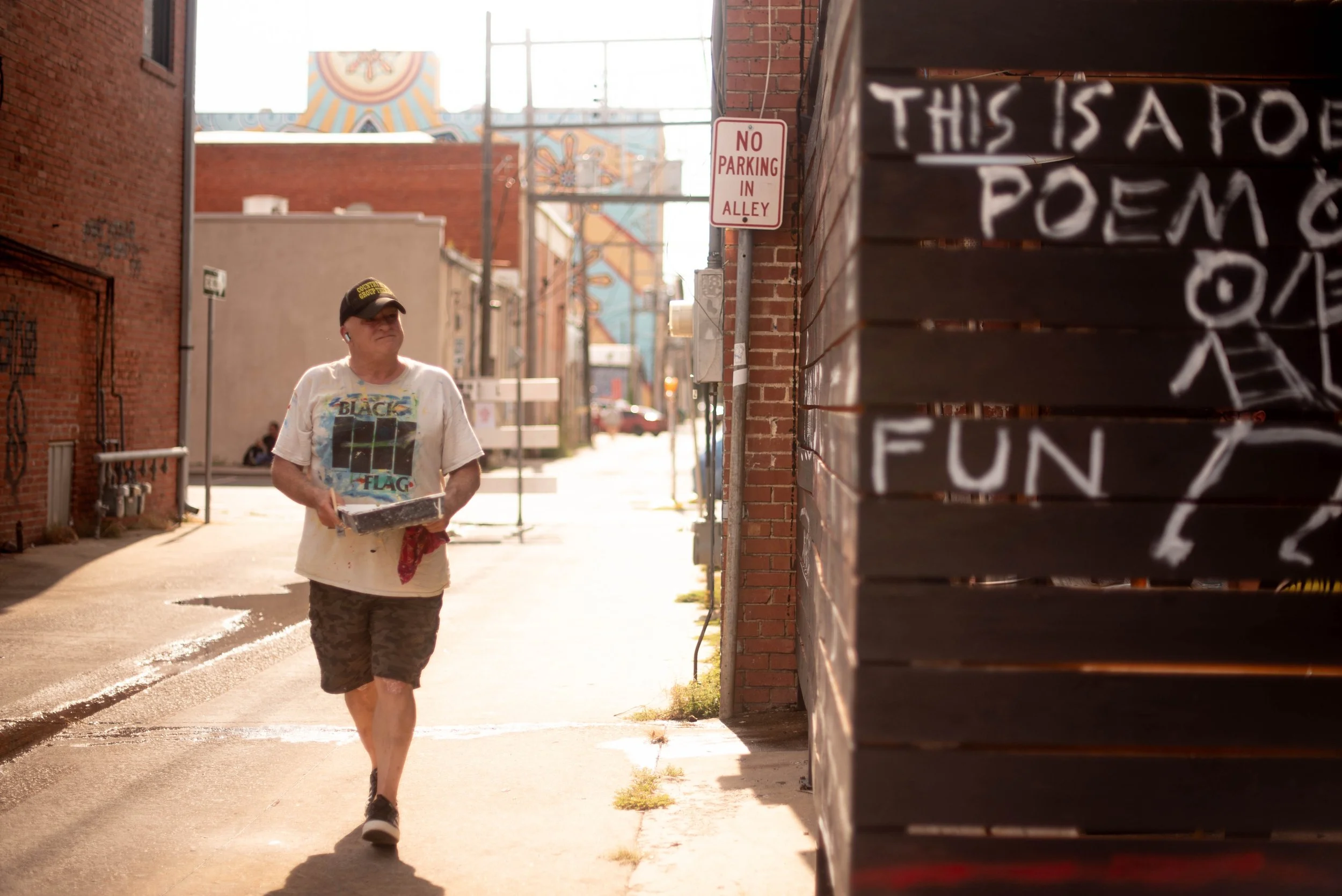 Barry Zimmerman holding paint and supplies while working on the fence of the Opolis during Ink the Block Party 2025