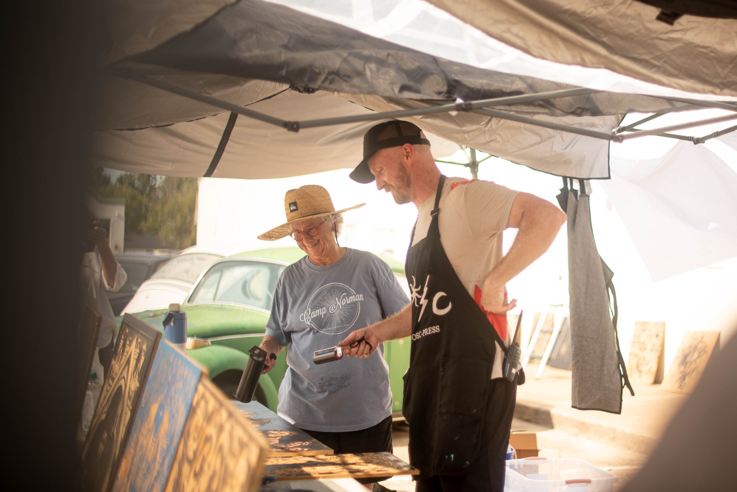 Two people in approns prepping blocks to print with a steam roller holding ink rollers and smiling