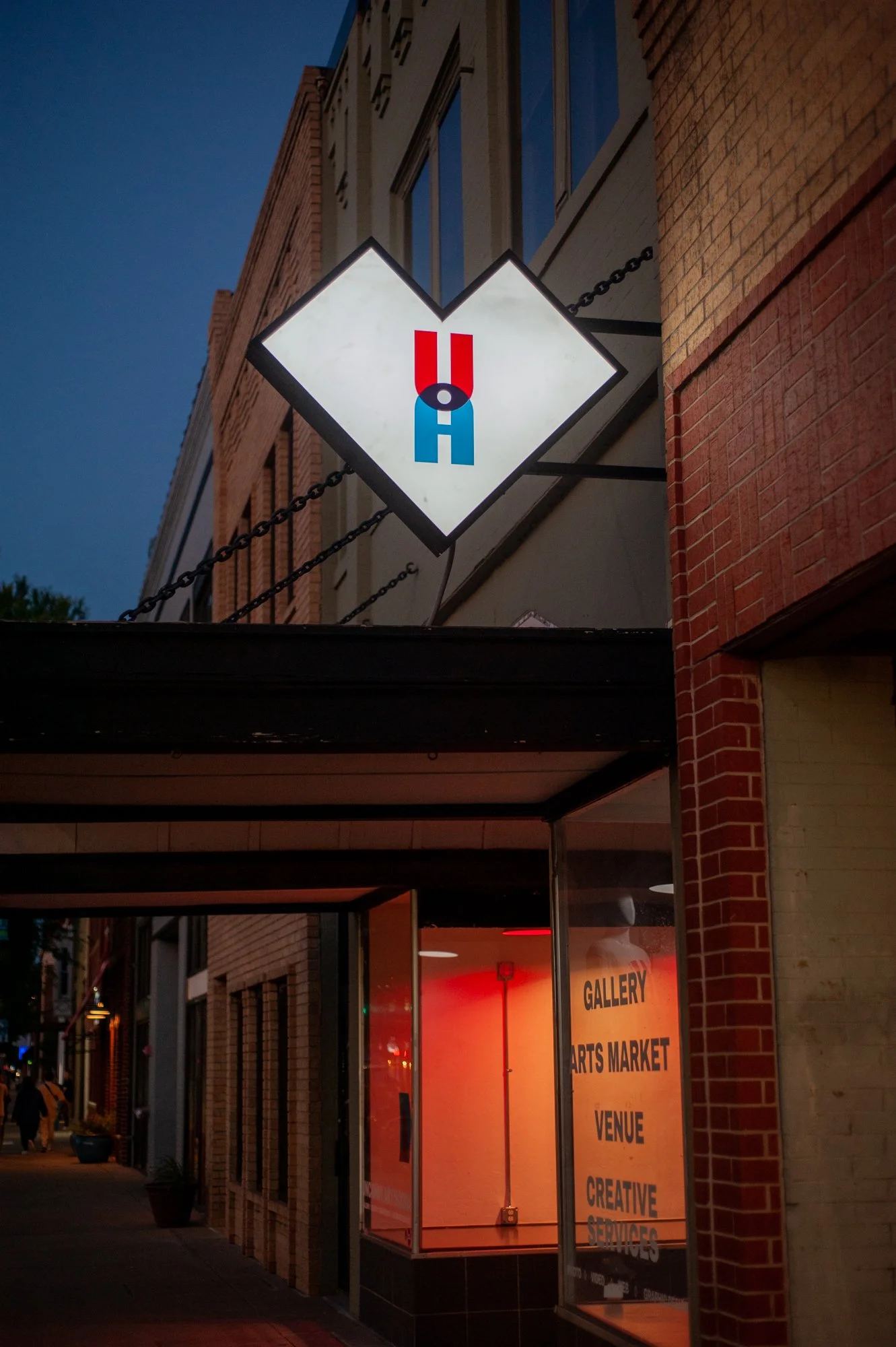 The front of Uncanny Art House with brick exterior and a glowing sign featuring an artistic U and A and a red-orange glow coming from the windows