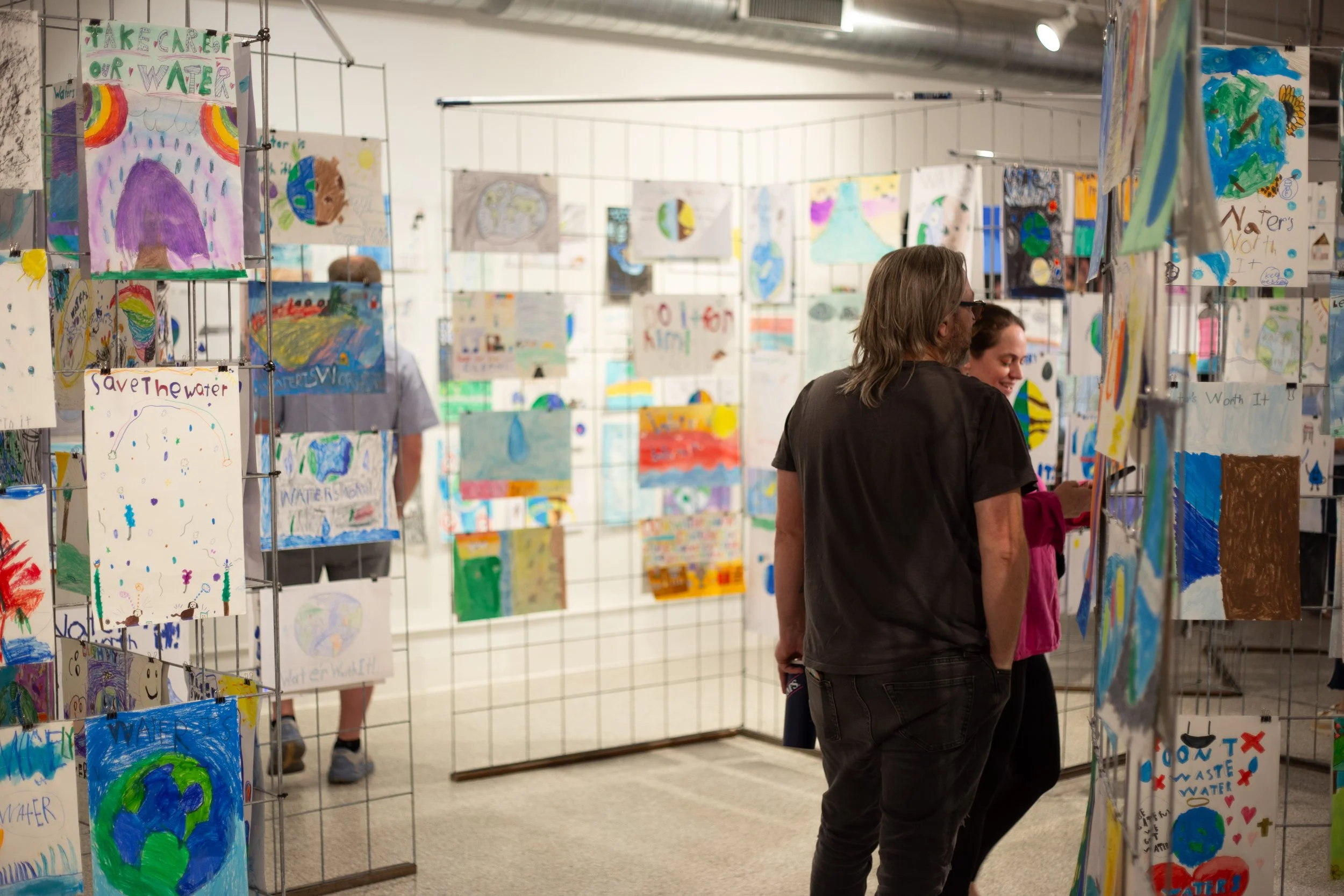 Two people walk through the gallery looking at posters to vote on