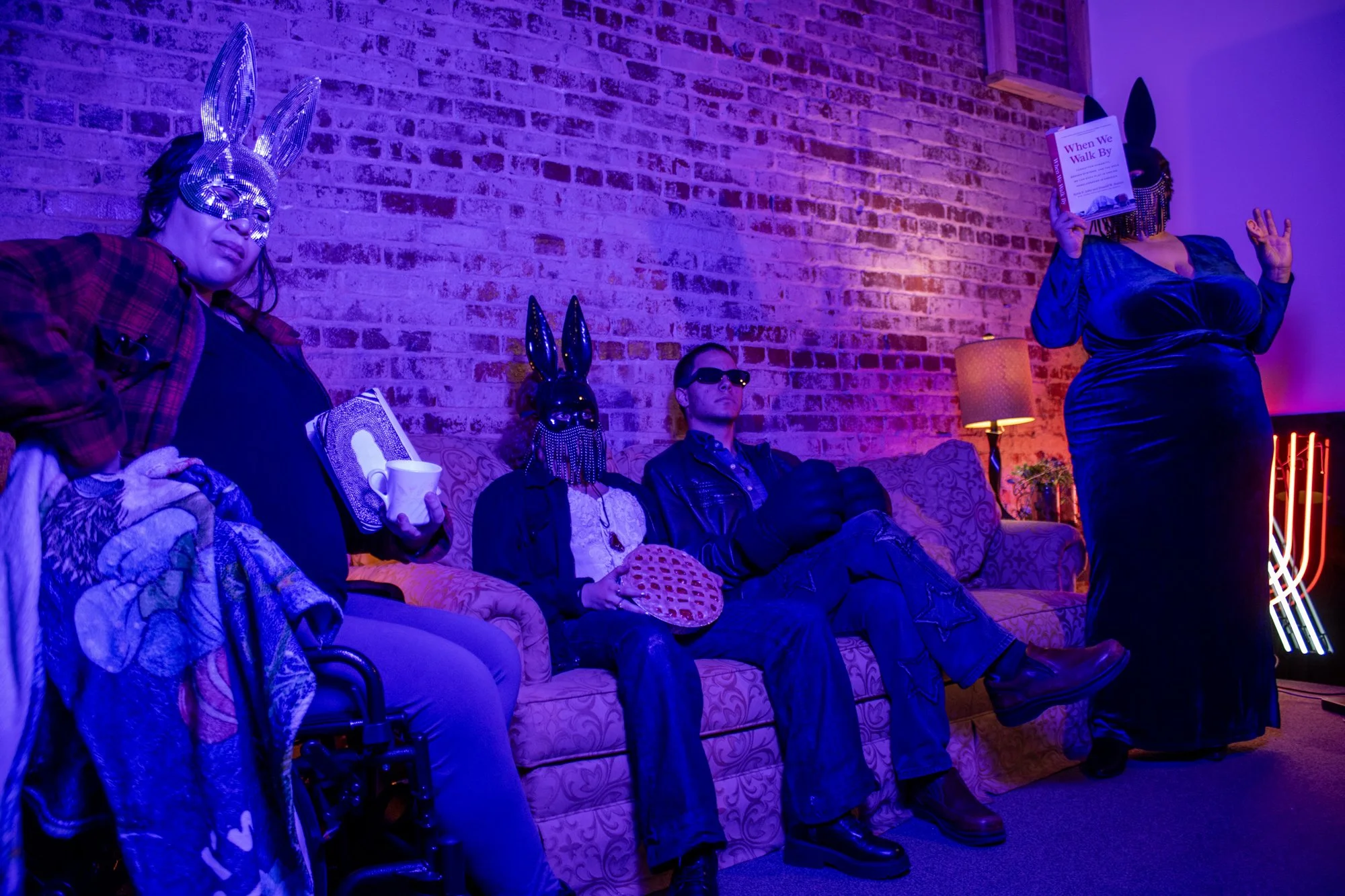 4 people in a living room sitting whereing bunny masks and interacting with props on a gold couch and a brick backdrop background in the Uncanny Art House photo studio