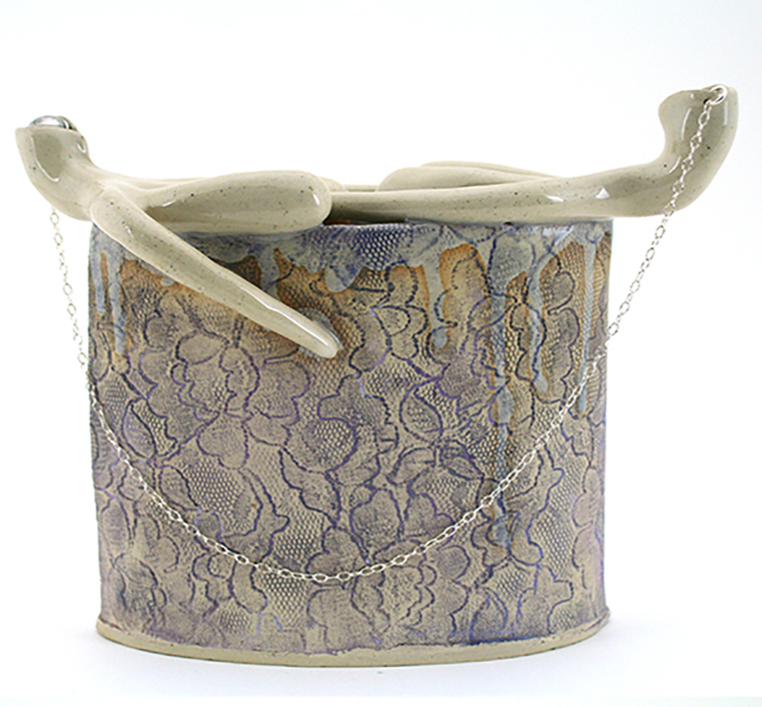 Clitoris Flower Brick is a cylindrical vessel wrapped in blue floral patterns and topped with two chain-linked clitoris forms. Designed to hold flowers, it celebrates and normalizes the clitoris.