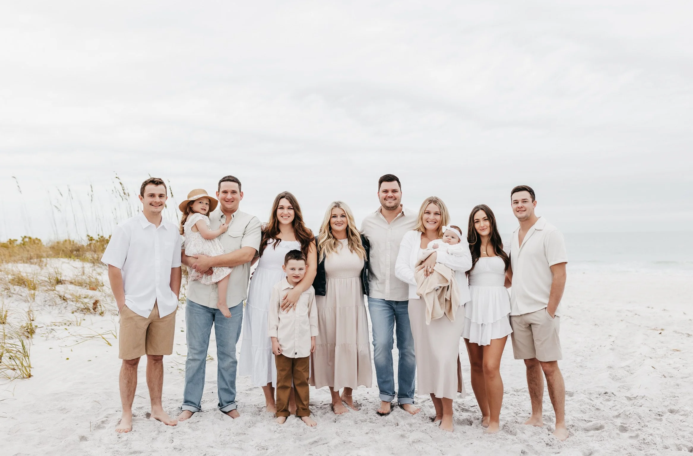 Family group picture on a beach, standing in a line and smiling at the camera.