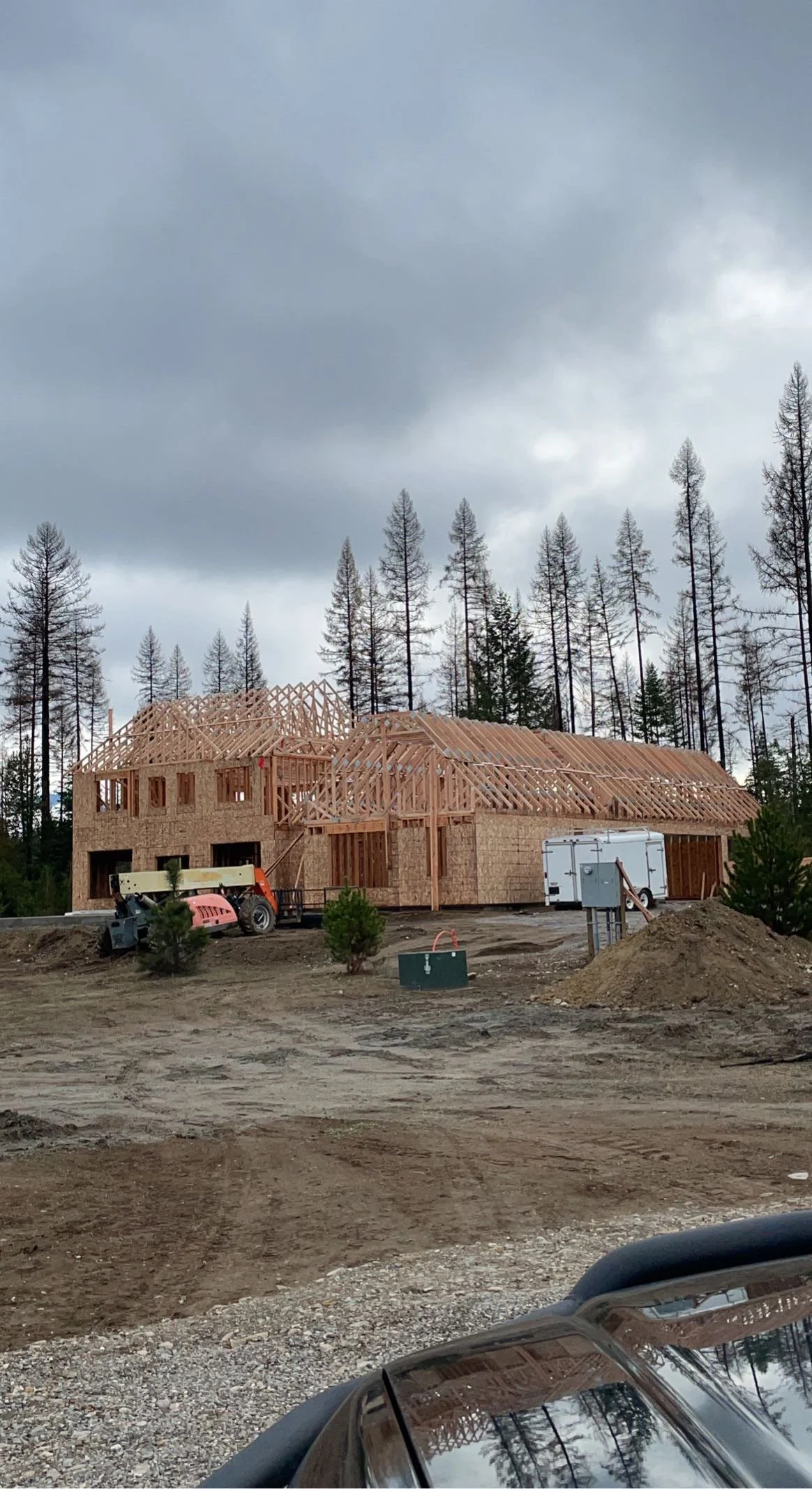 Construction site with wooden framework of a house under overcast skies, surrounded by trees.