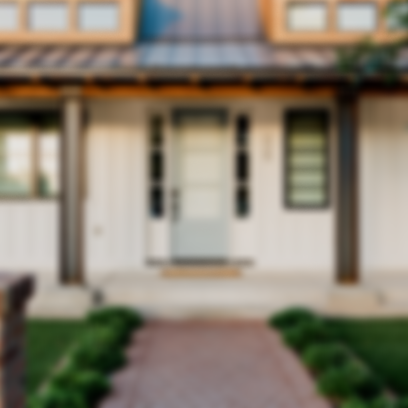 A blurry front porch of a house with a path leading to the steps, green bushes on each side of the path, and windows on the upper floor.