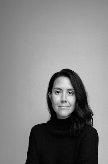 Black and white portrait of a woman with shoulder-length wavy hair, wearing a black turtleneck sweater, looking at the camera with a slight smile.