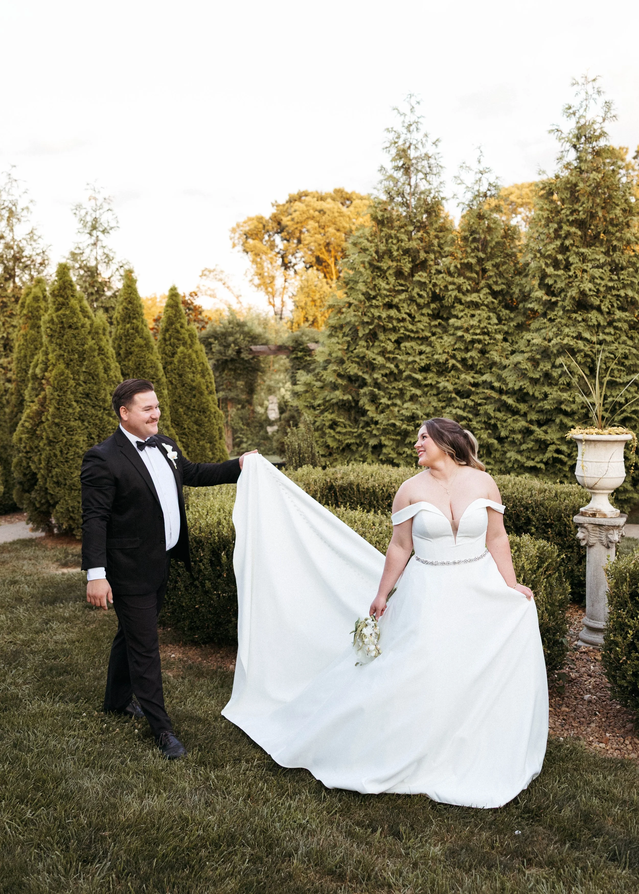 Groom is holding bride's train for her as the bride looks back to admire her groom in a Kentucky courtyard