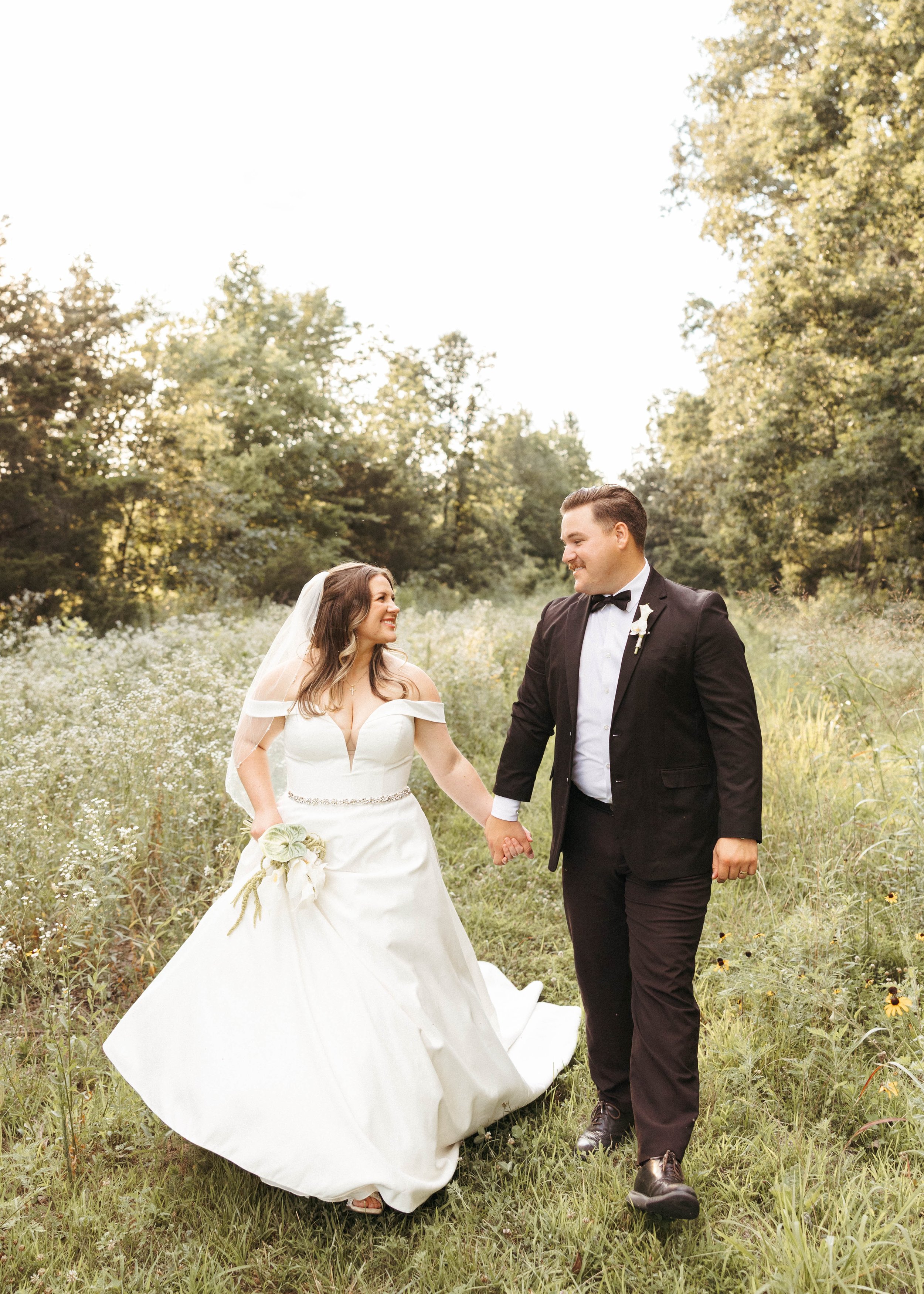 bride and groom walk hand in hand across a wildflower field in Kentucky while taking bride and groom portraits