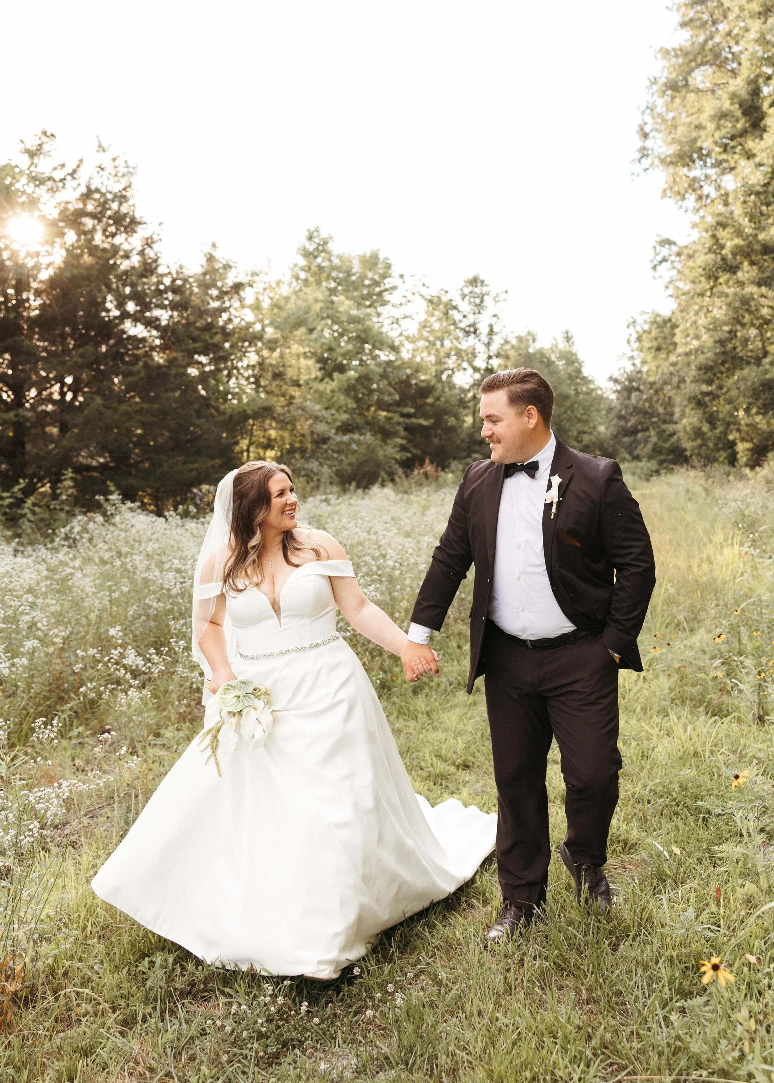 Bride and Groom walk through a field of wildflowers admiring each other hand in hand