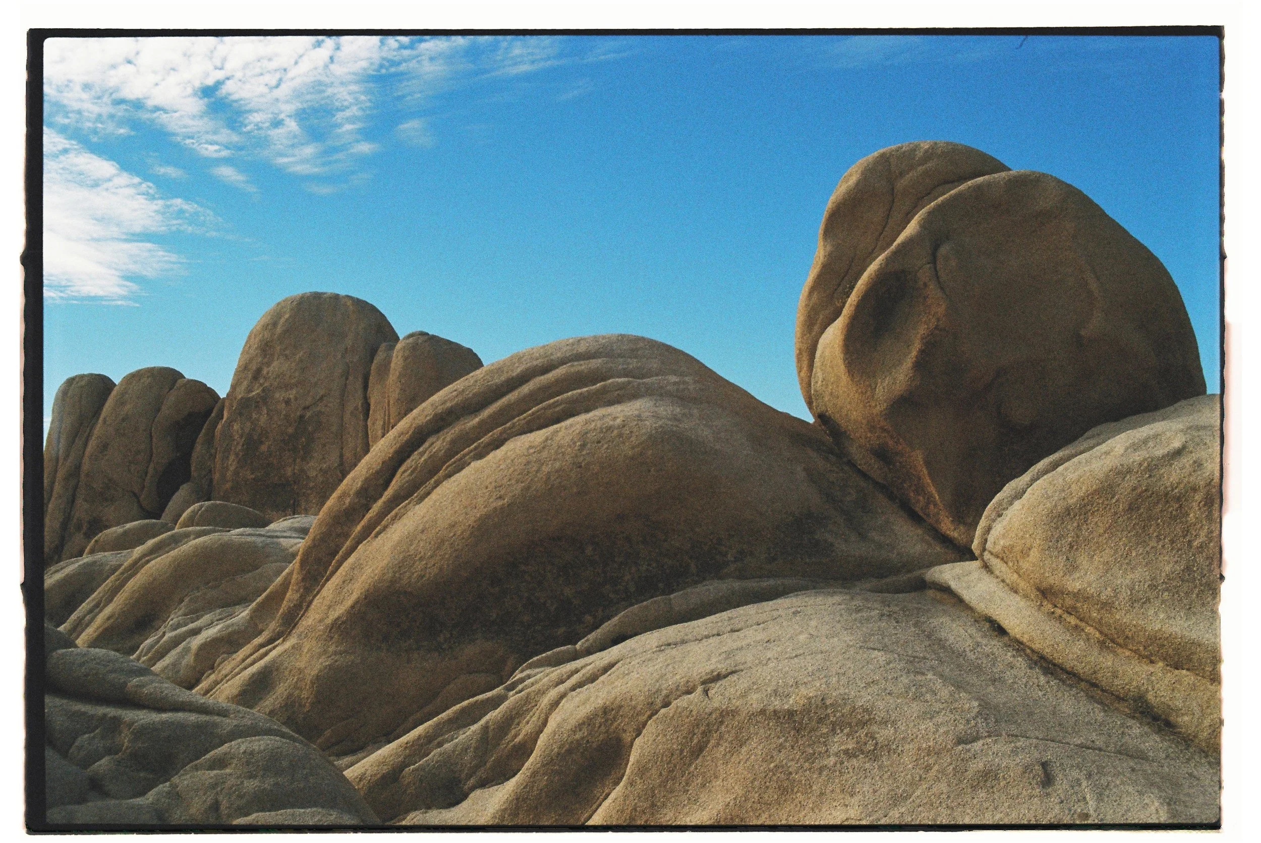 Large weathered granite boulders stacked on each other under a blue sky with wispy clouds.