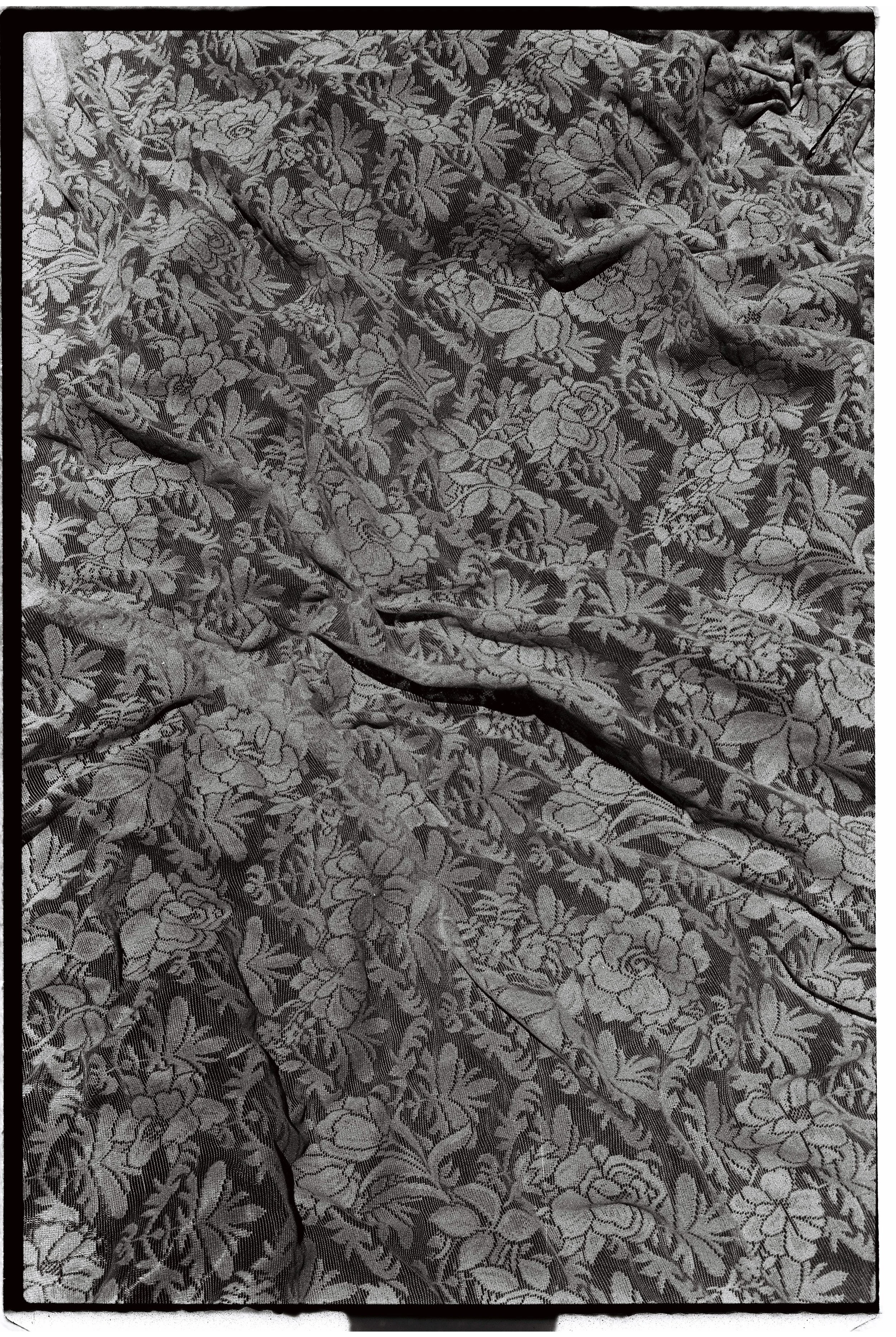 Close-up of a fabric with a floral pattern in shades of black and gray, with some wrinkles and folds.