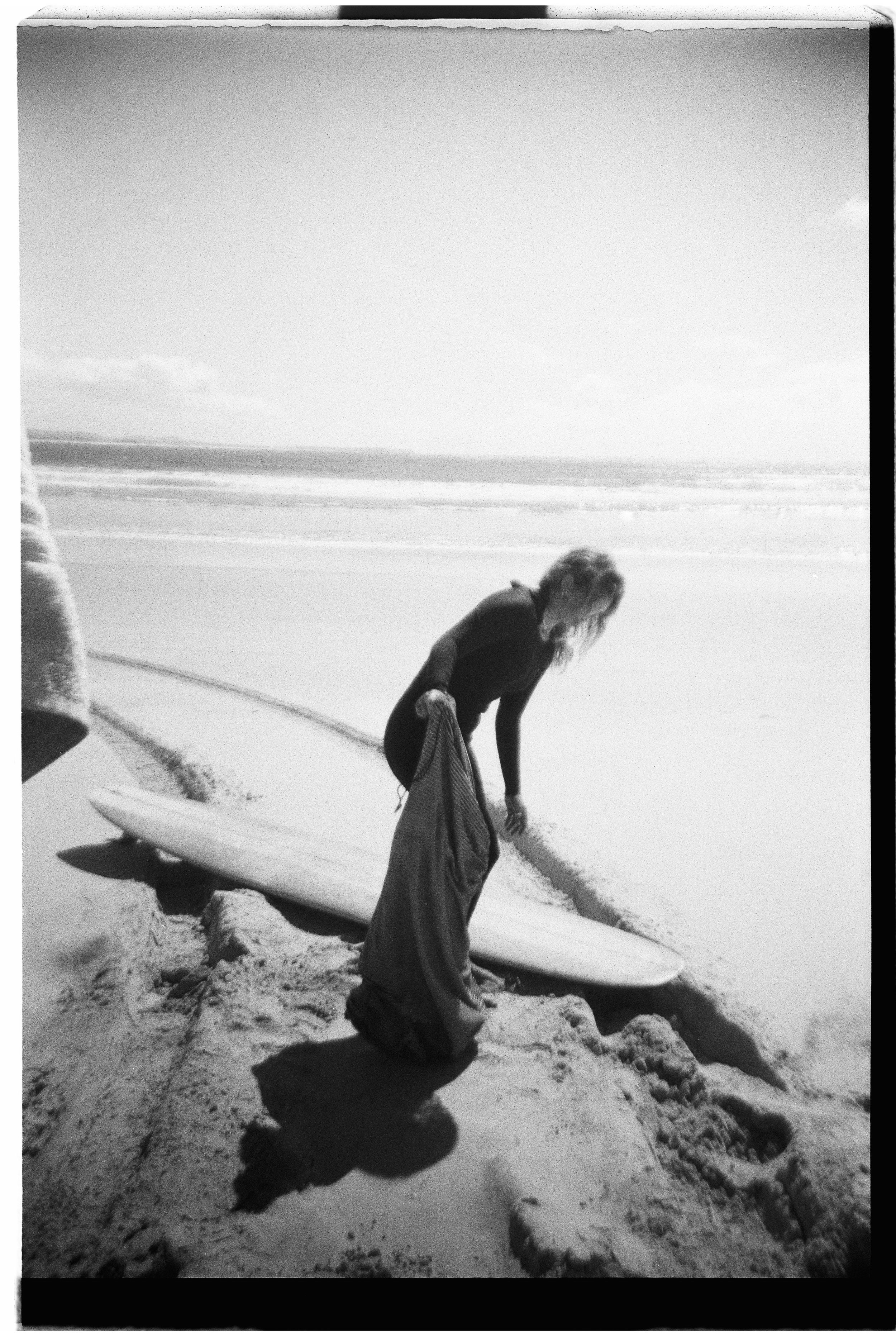 A woman in a wetsuit on a beach, preparing to surf, with the ocean in the background.